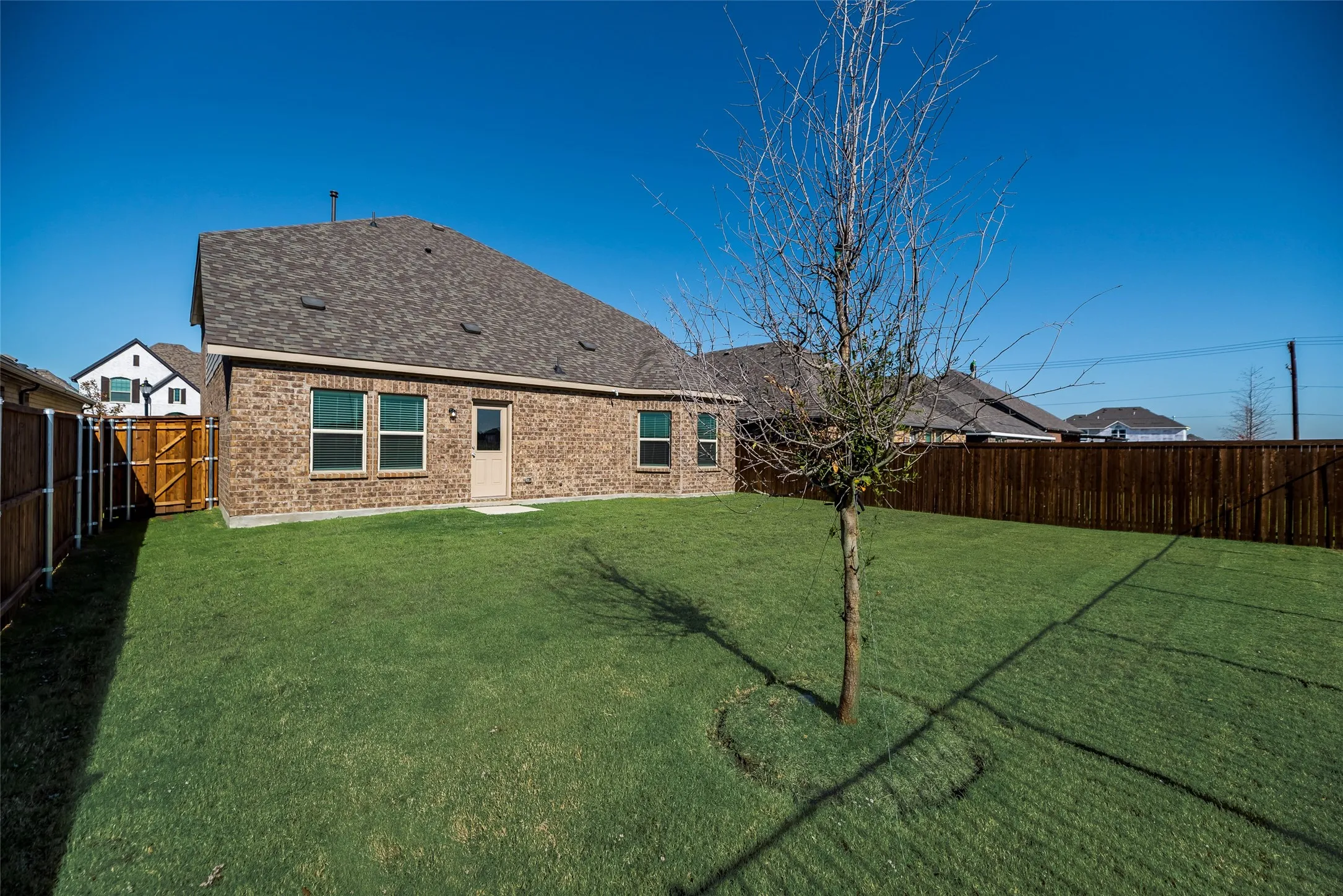 Expansive backyard featuring a manicured lawn, brick exterior, and a privacy fence