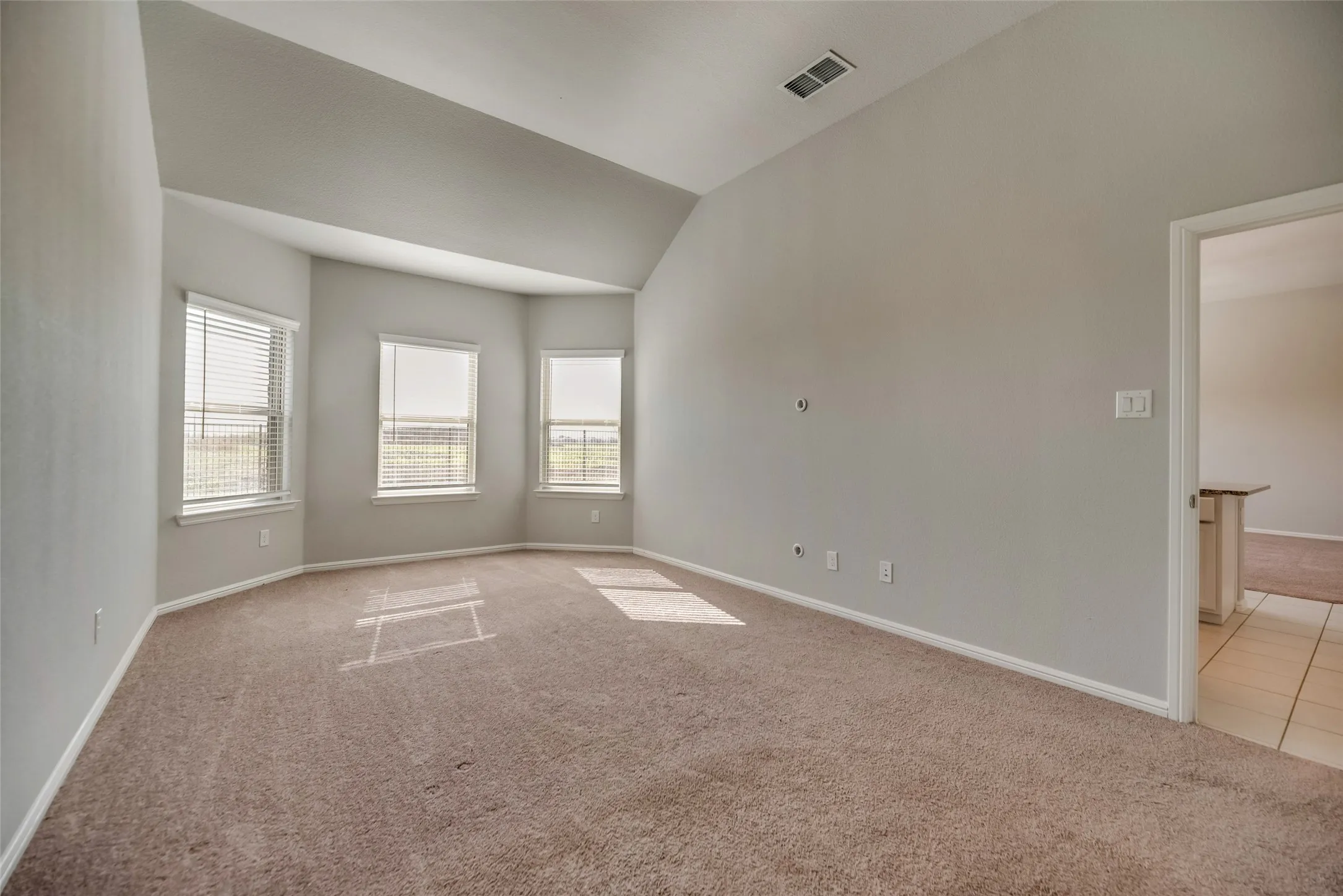 Vaulted ceiling, bay window, carpeted flooring, window blinds, and neutral wall tones