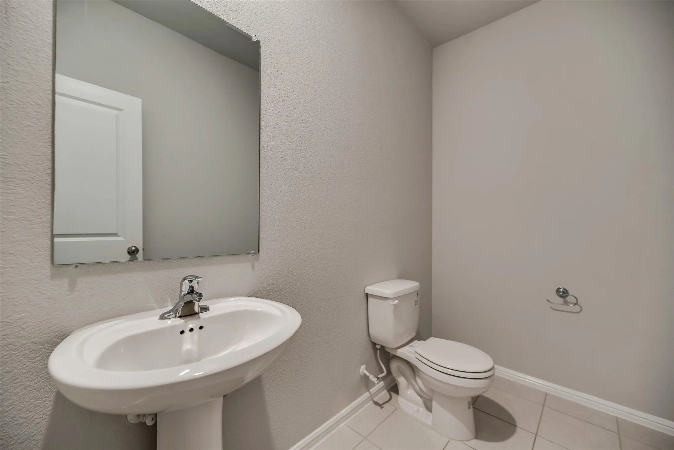 Pedestal sink with chrome faucet, wall-mounted mirror, and tile flooring