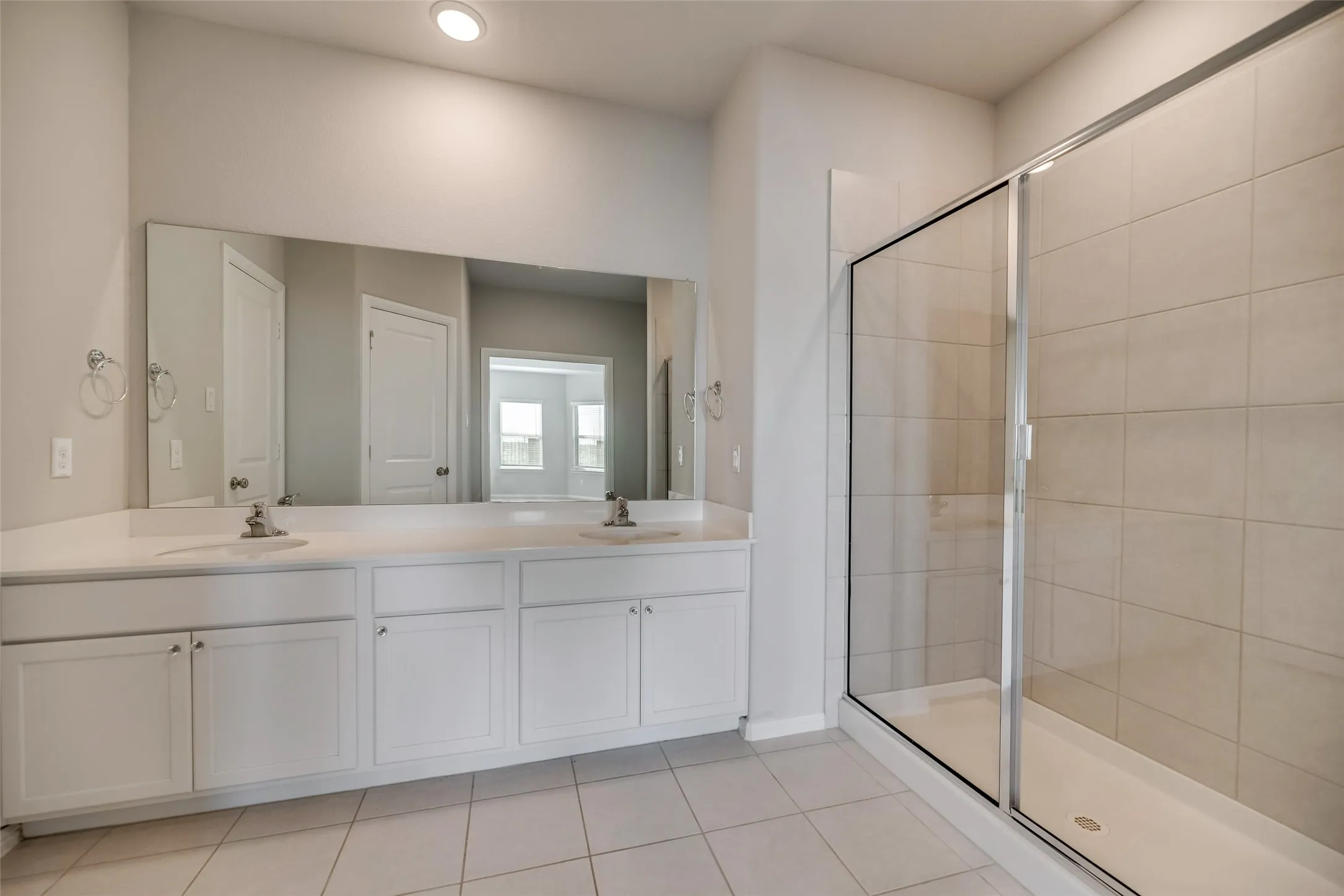 Dual vanity with white cabinetry and integrated sinks, a frameless glass shower enclosure, large format wall tiling, and recessed lighting