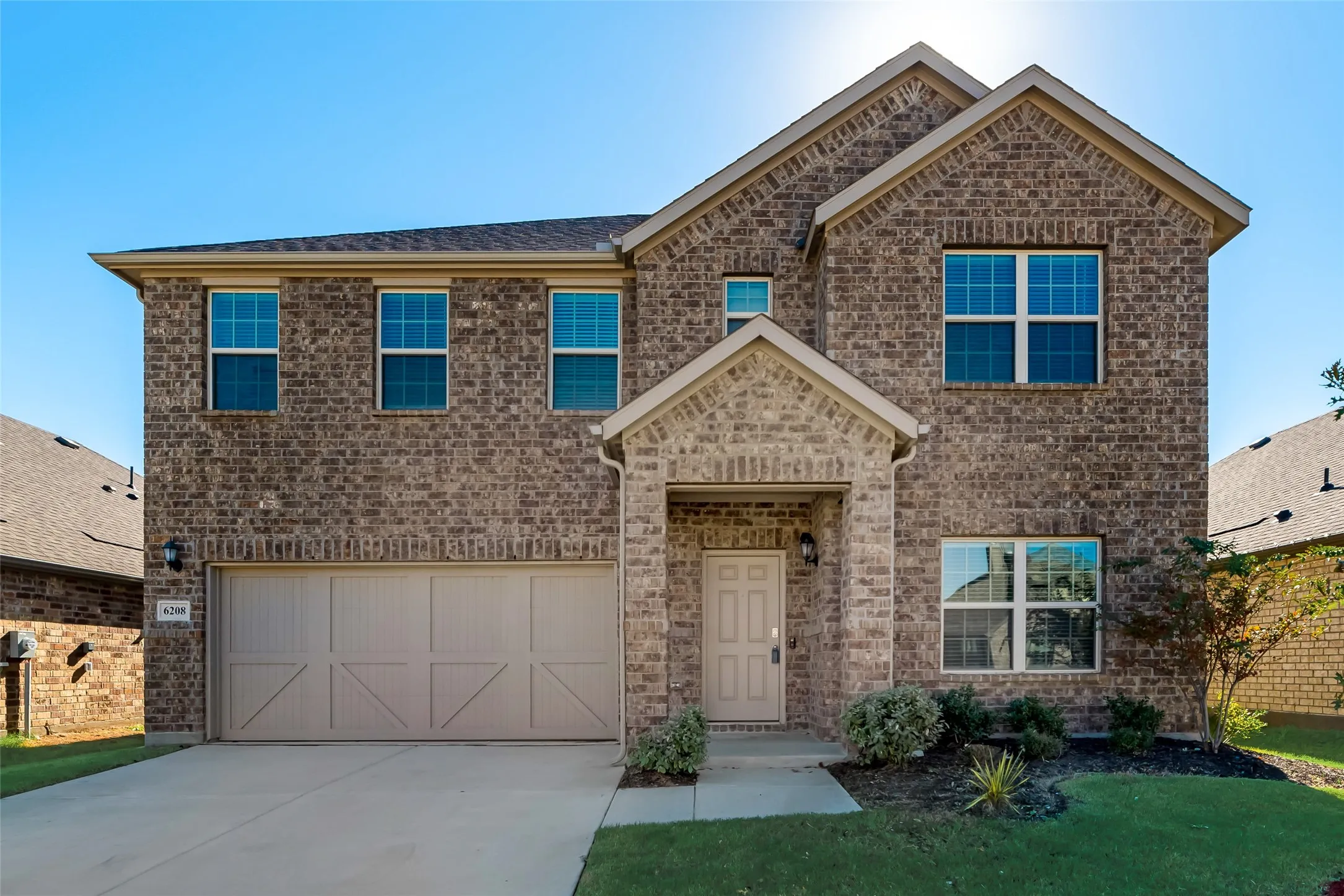 Two-story brick exterior with gabled roofline, attached two-car garage, covered entry, and established landscaping
