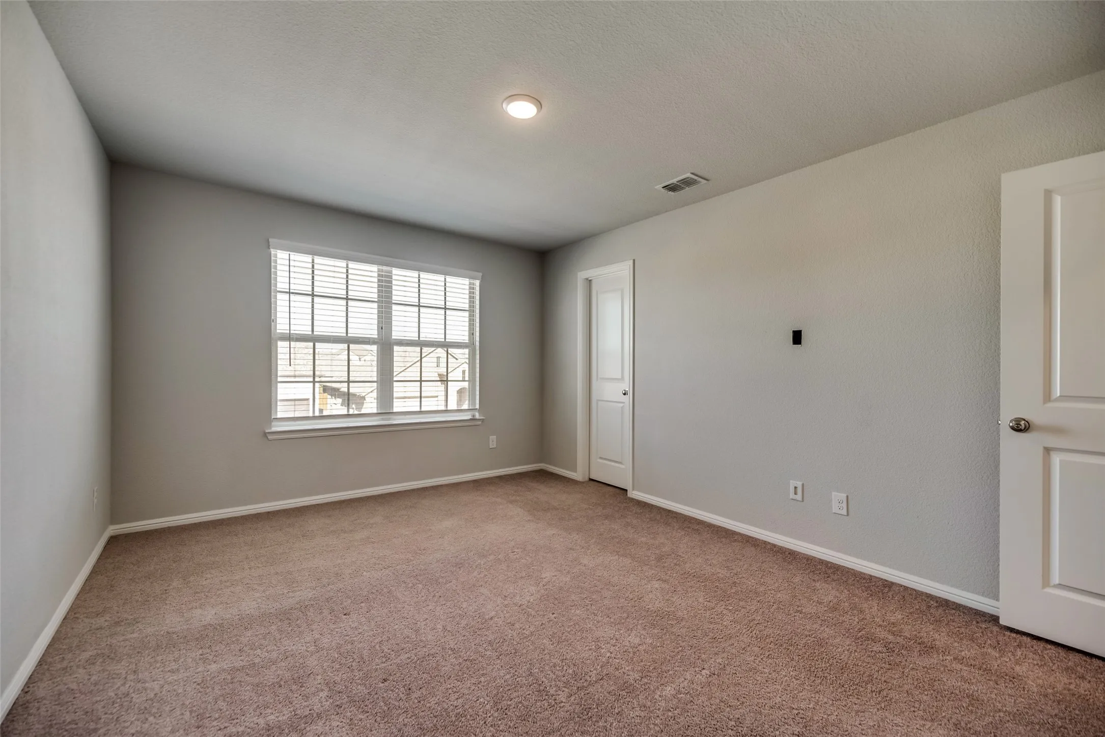 Neutral tone wall paint, recessed ceiling lighting, carpet flooring, window with blinds, and white interior doors