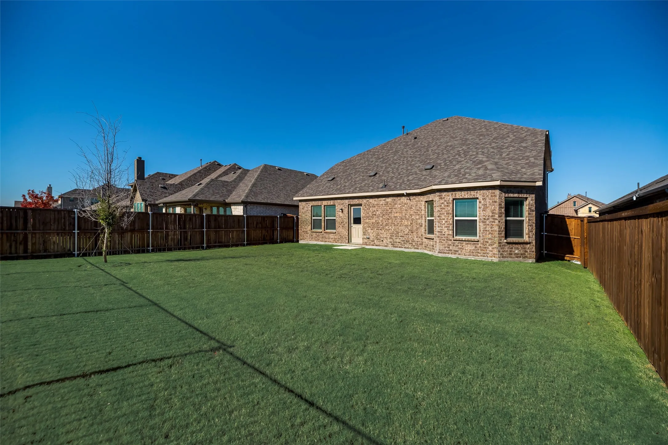 Expansive backyard featuring a manicured lawn, full brick exterior, and a privacy fence