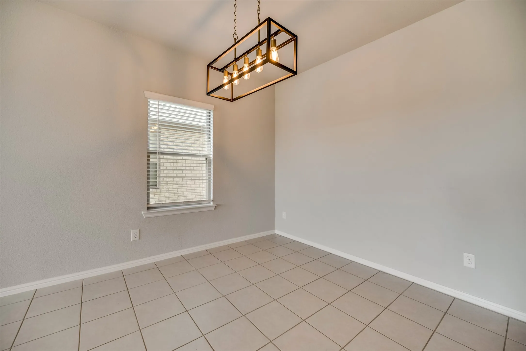 Recessed window with blinds, overhead linear chandelier, and tile flooring