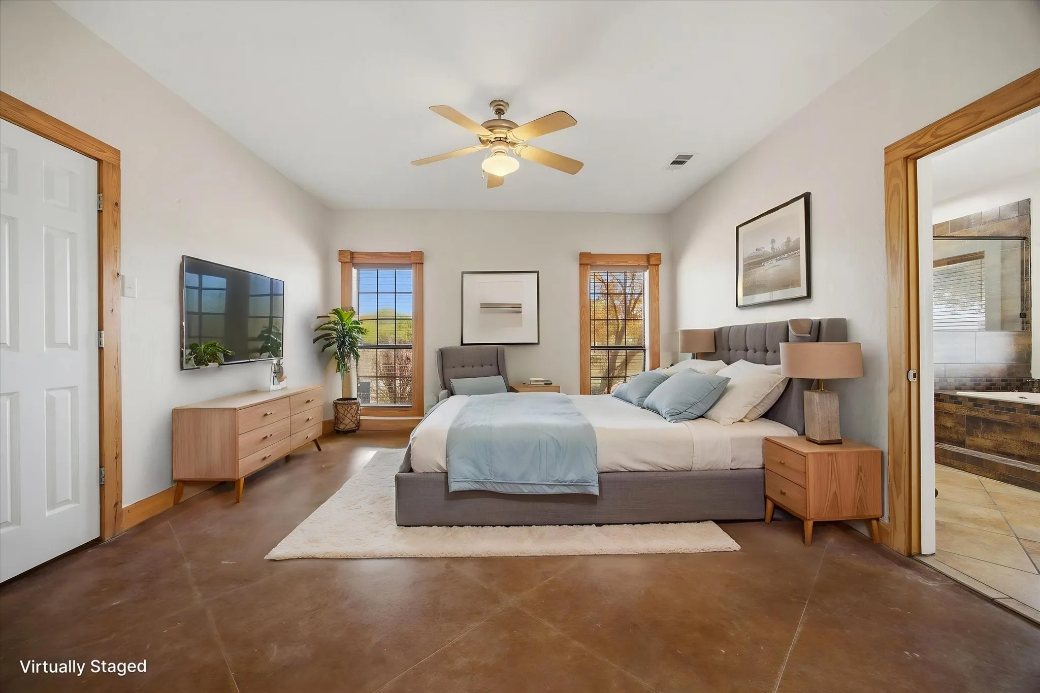 Virtually staged. Large primary bedroom with ensuite spa bath and stained concrete flooring.