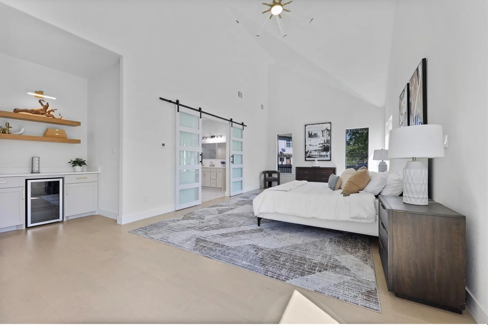 Vaulted ceilings with a modern ceiling light fixture, wood-finish flooring, built-in cabinetry with a beverage refrigerator, and barn doors with frosted glass panels
