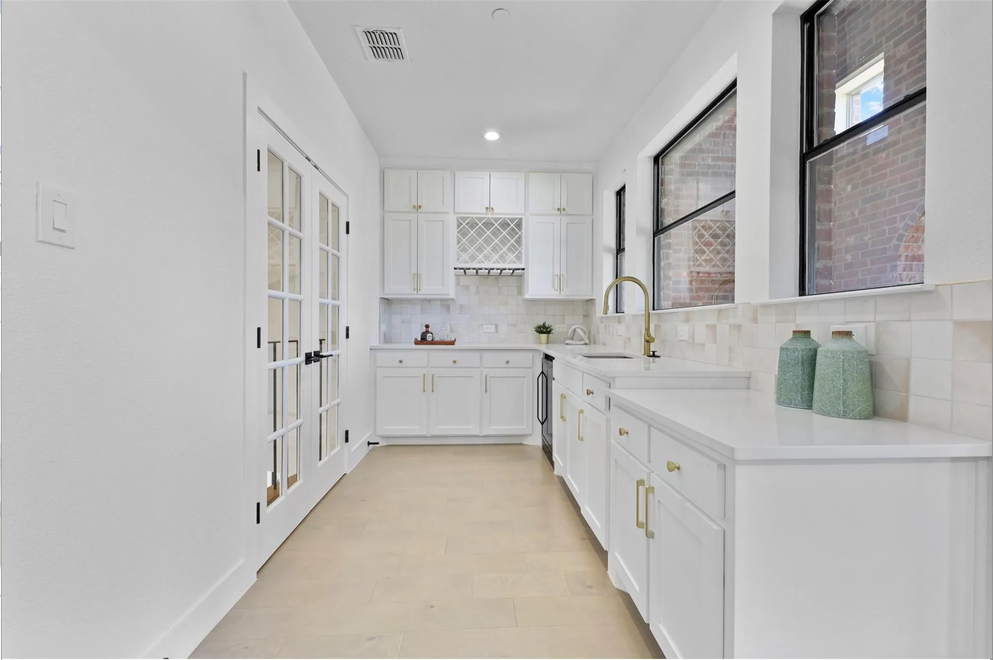 White cabinetry, light wood-finish flooring, white countertops, built-in wine rack, and a tile backsplash