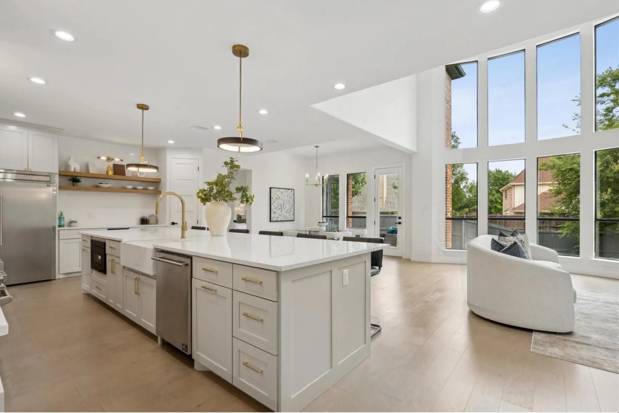 Gourmet kitchen with a large central island, white cabinetry, integrated stainless steel appliances, and wood-finish flooring