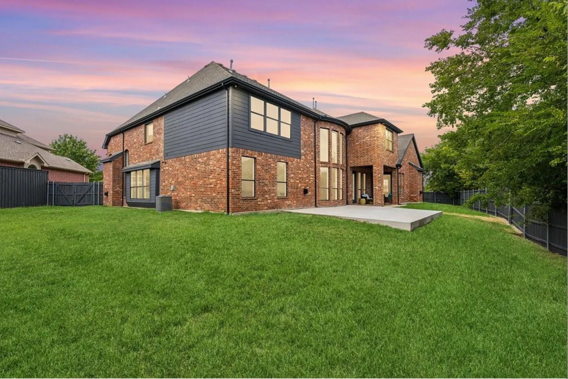 Expansive backyard featuring a manicured lawn, a large concrete patio, and a brick and dark-paneled exterior