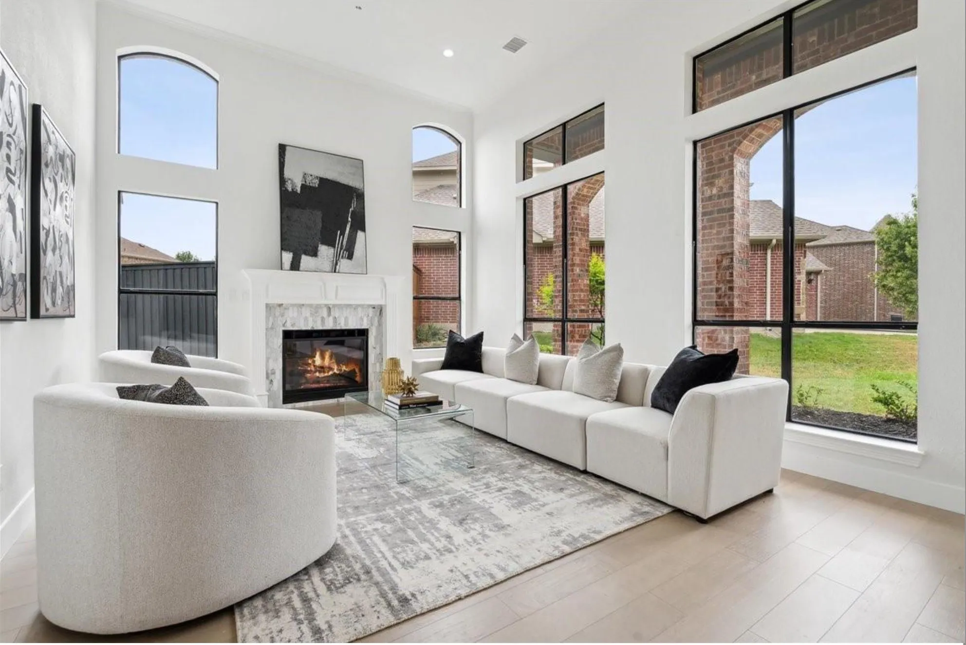Soaring ceilings, expansive window arrangements, wood-finish flooring, and a fireplace with a tile surround and mantel