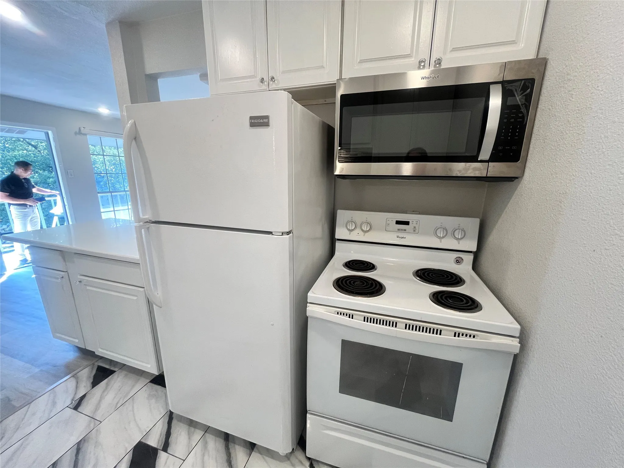 White cabinetry with brushed nickel hardware, stainless steel microwave, white range, white refrigerator, and a white countertop