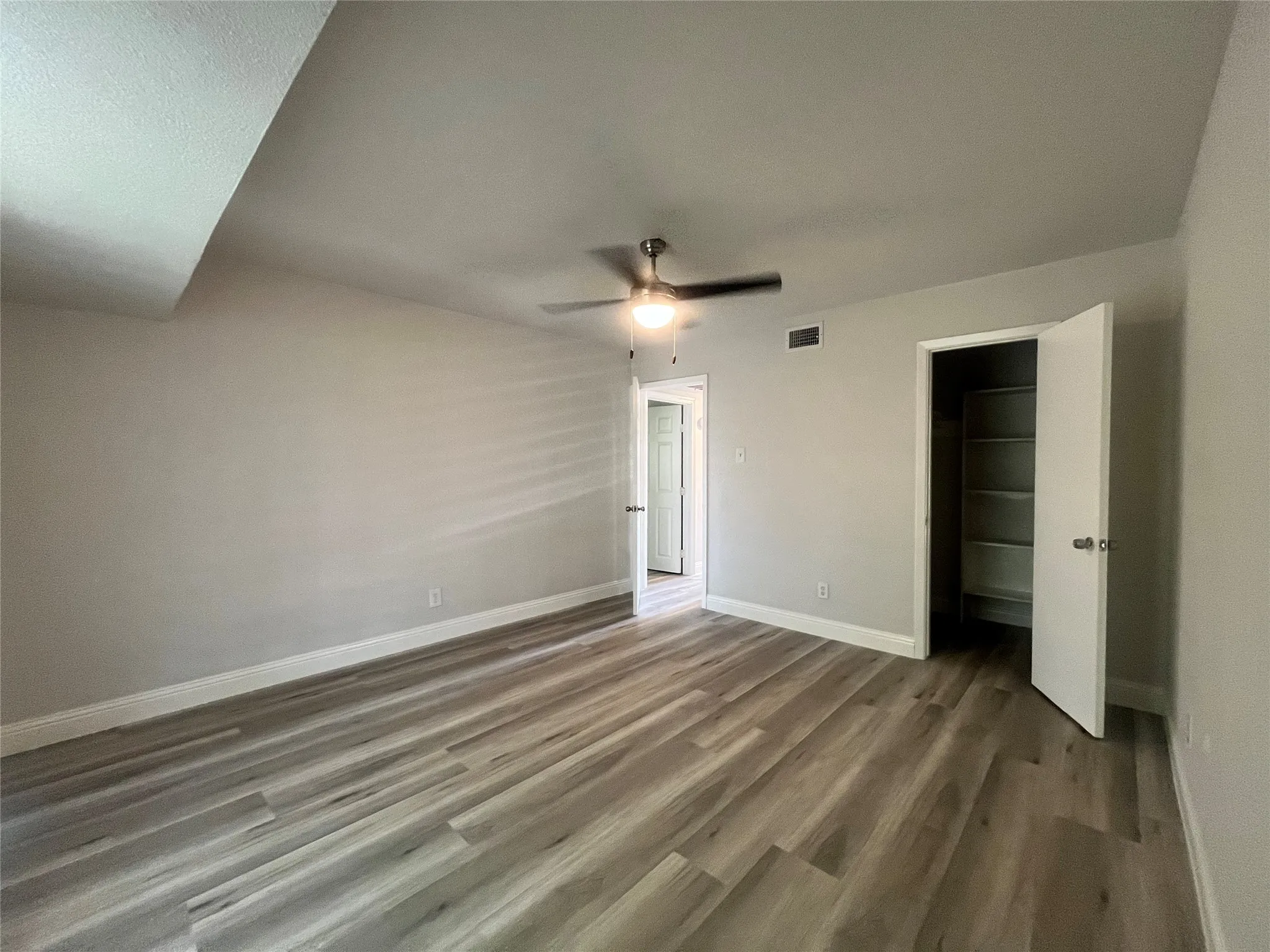 Spacious room featuring wood-finish flooring, a ceiling fan with integrated lighting, and a built-in closet with shelving