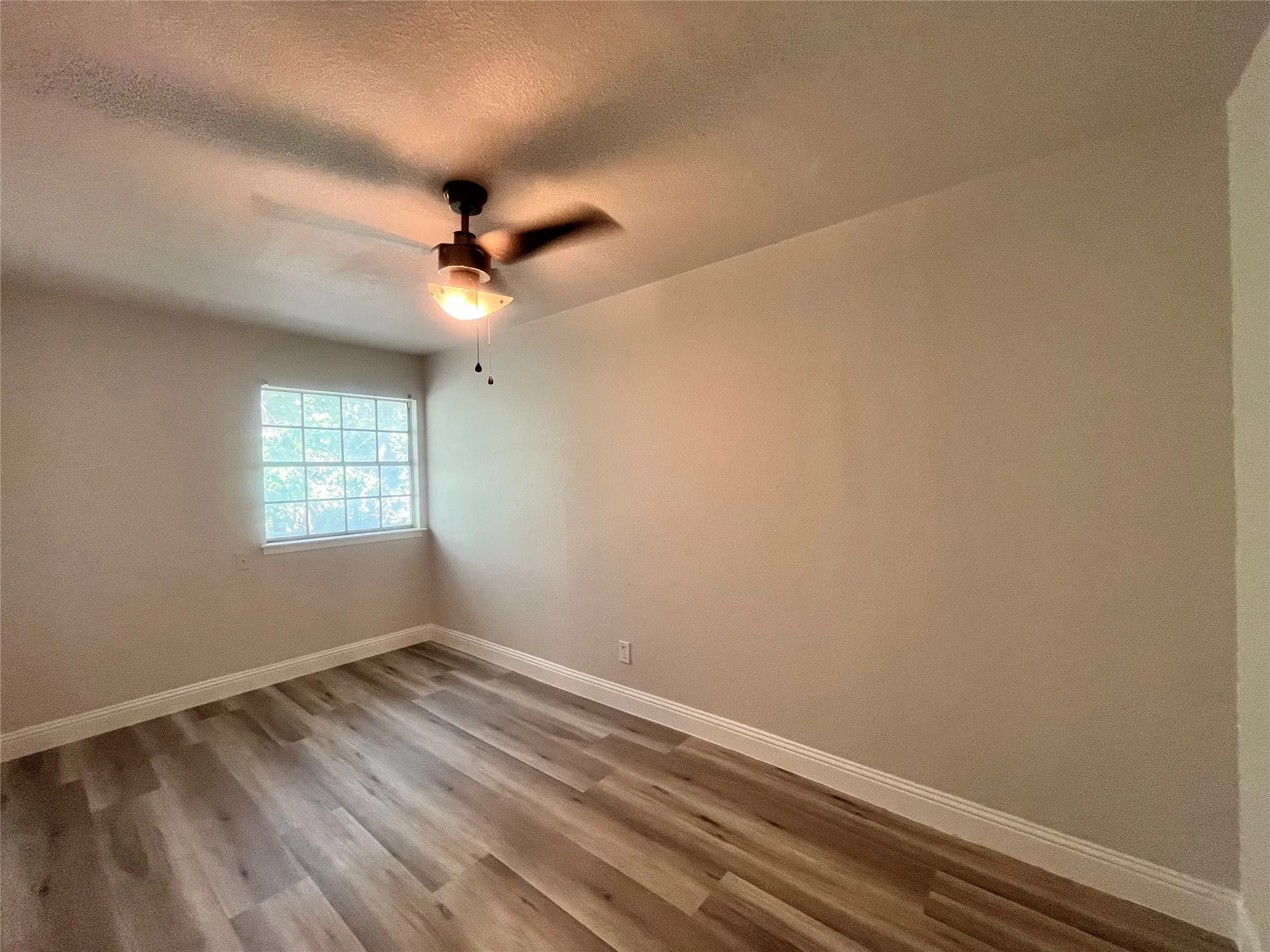 Wood-finish flooring, white baseboards, and a ceiling fan with integrated lighting
