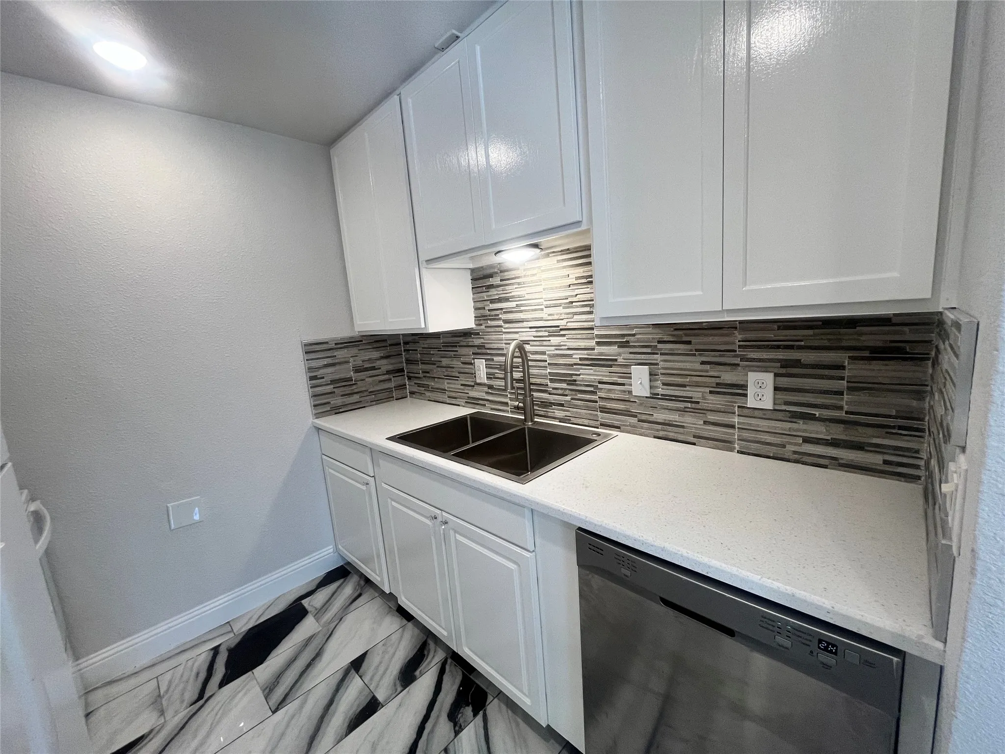 Kitchen featuring white cabinetry, a dual-basin stainless steel sink with a gooseneck faucet, light-toned countertop, and a mosaic tile backsplash