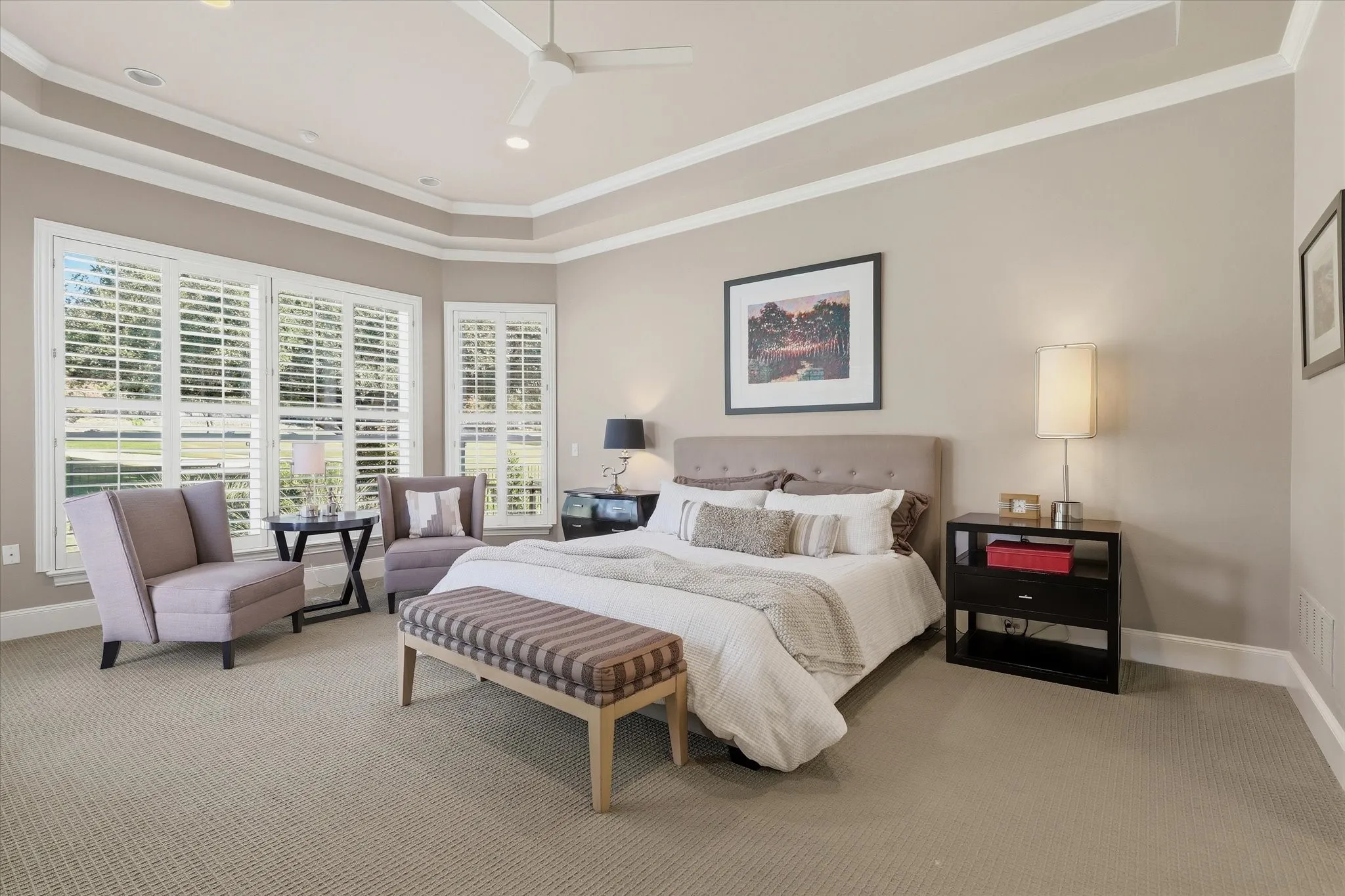 The secluded primary suite offers a tranquil retreat, with a layered tray ceiling, sitting area and picturesque outlook across the green.
