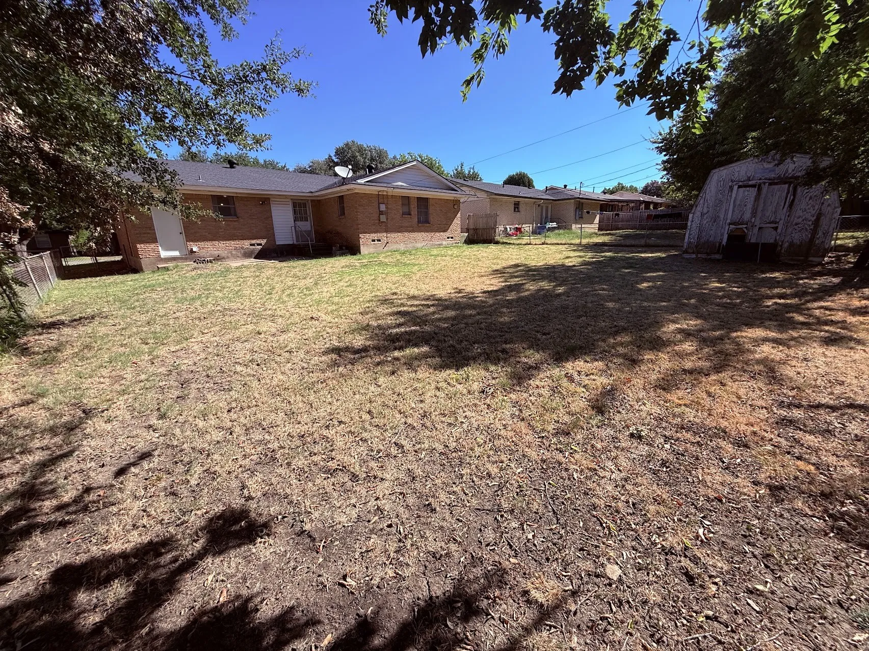 Brick exterior, white entry doors, black shingle roof, mature trees, fenced perimeter