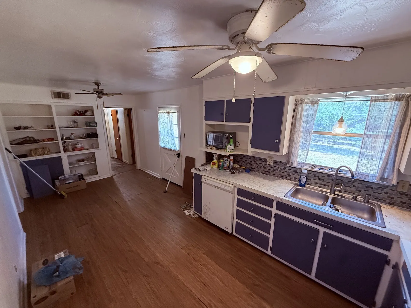 Kitchen featuring wood-finish flooring, built-in shelving, blue cabinetry, a stainless steel double-basin sink, and a mosaic tile backsplash