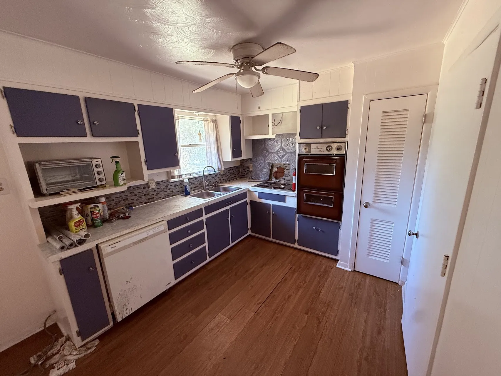 L-shaped kitchen with wood-finish flooring, two-tone cabinetry, and built-in double oven