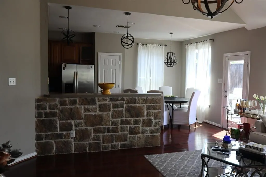 Stone-clad breakfast bar, wood-finish flooring, recessed kitchen area, French door access to the exterior, and suspended light fixtures