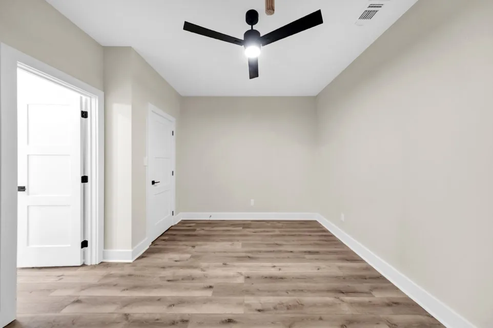 Wood-finish flooring, white paneled doors with matte black hardware, a ceiling fan, and white trim molding