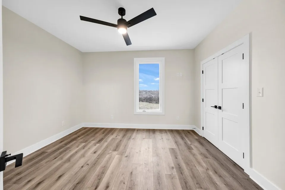 Neutral tone walls, wood-finish flooring, modern ceiling fan, white trim, and a window with natural light