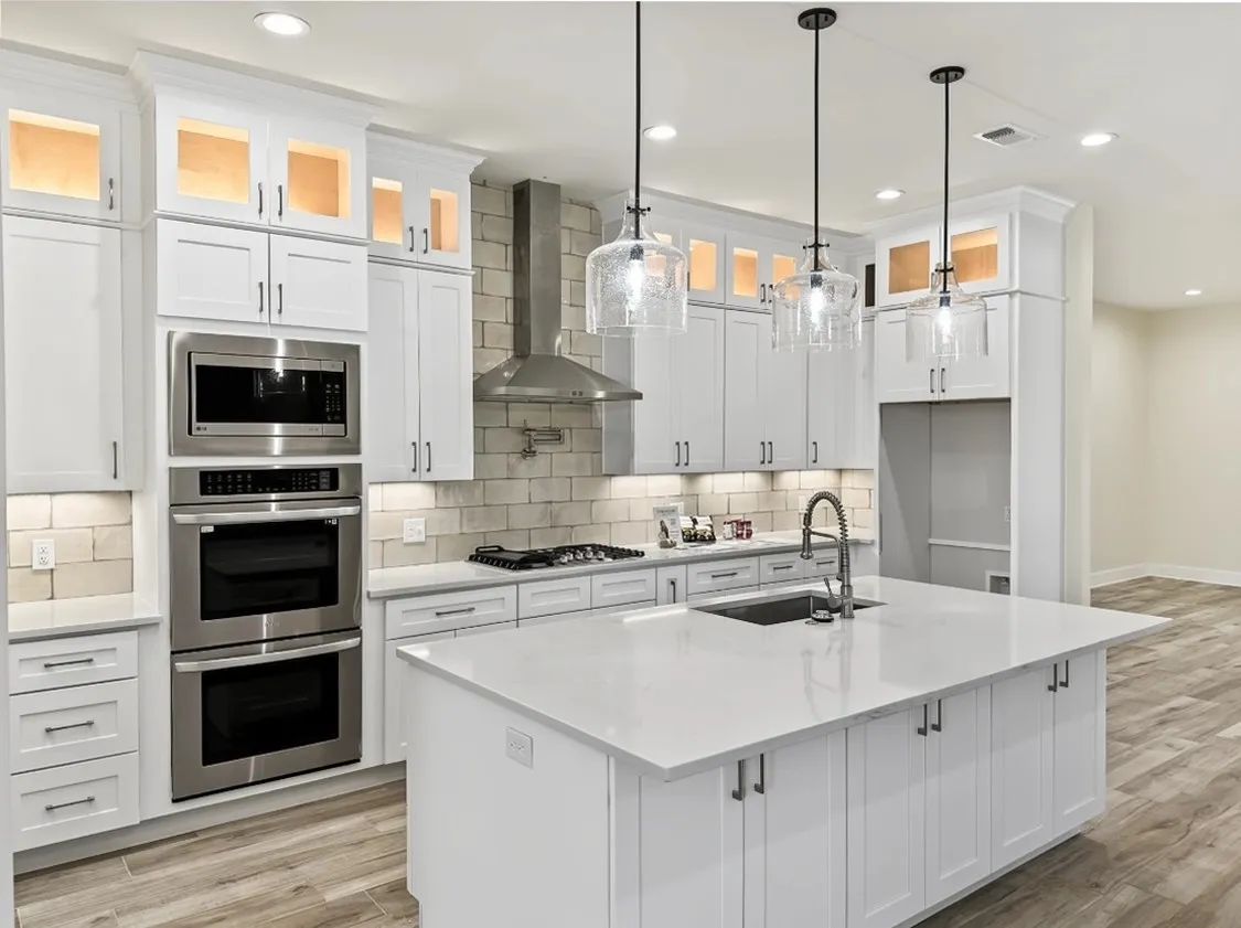 White cabinetry with glass-front upper cabinets, stainless steel appliances, a center island with an undermount sink, pendant lighting, and wood-finish flooring