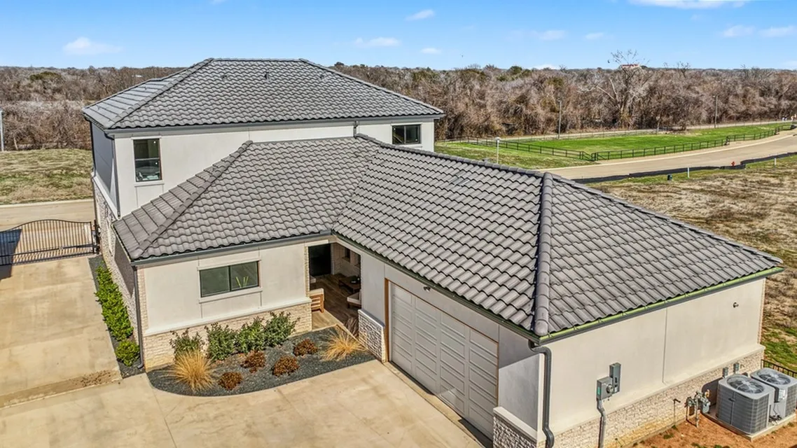 Stucco exterior with a tile roof, a private gated entrance, an attached garage, and stone detailing