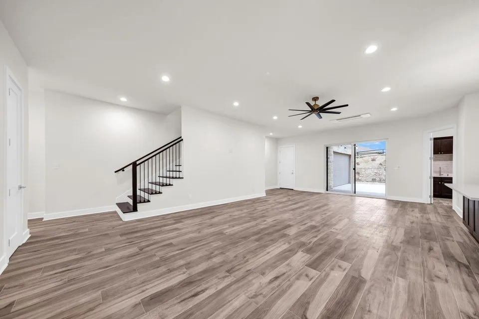 Open-concept living area featuring wood-finish flooring, a modern black railing staircase, recessed lighting, and a ceiling fan