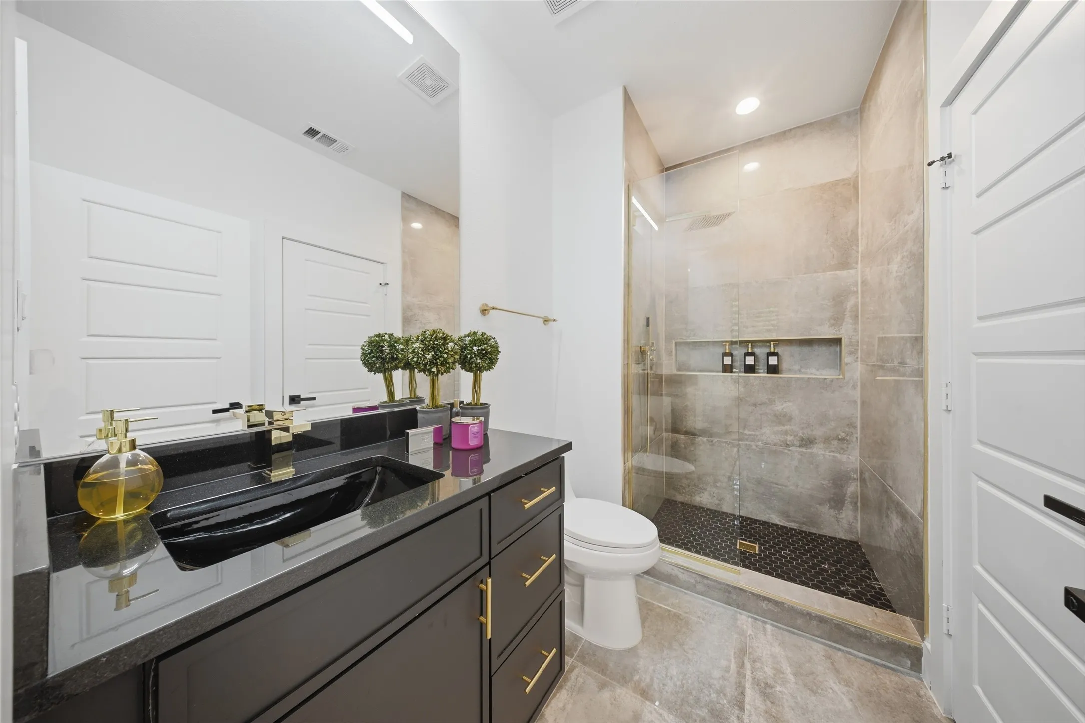 Spacious bathroom featuring a dark vanity with gold-tone hardware, a black vessel sink, and a glass-enclosed shower with tiled walls and a recessed niche