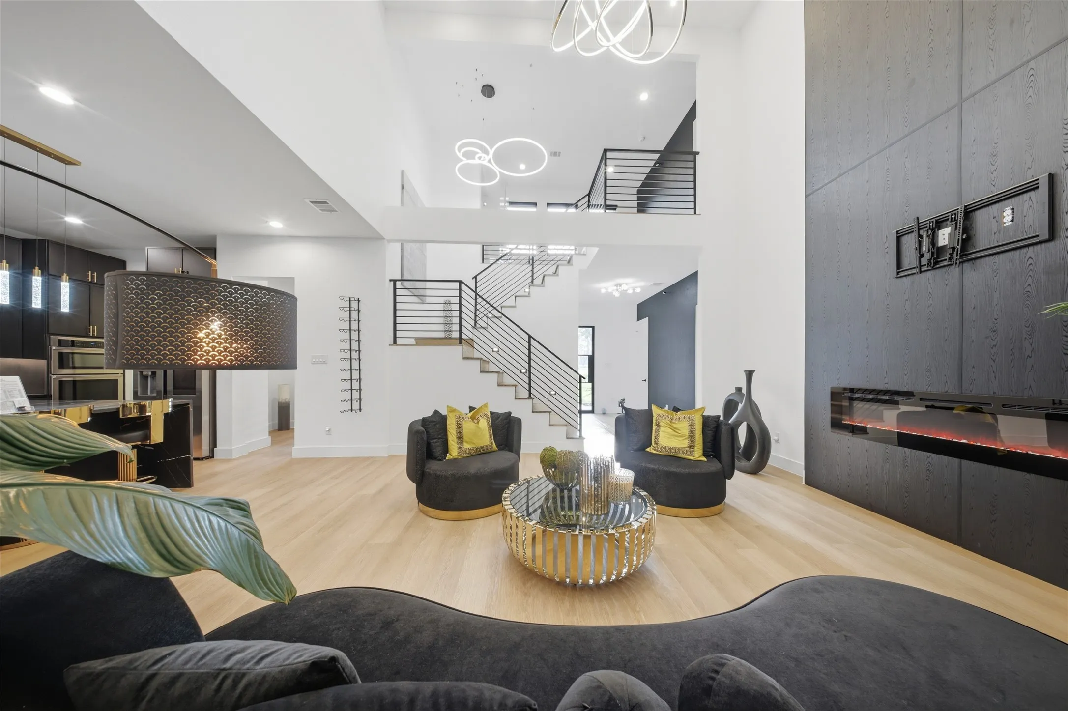 High ceilings, wood-finish flooring, two-story staircase with horizontal metal railings, modern linear fireplace, and contemporary lighting fixtures