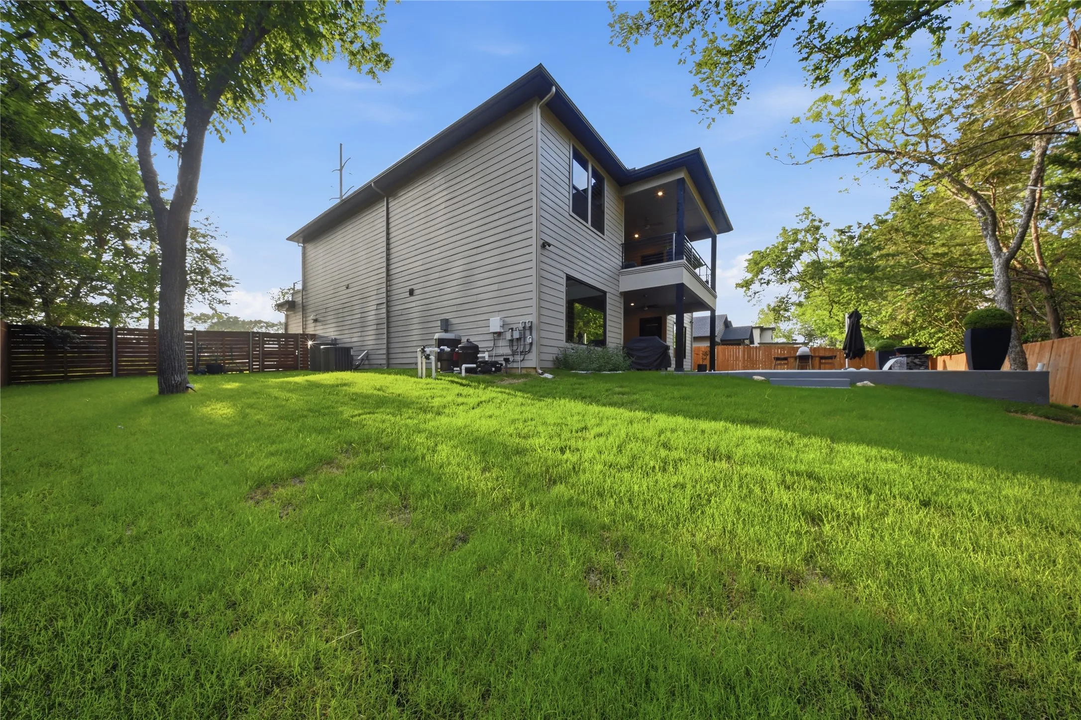 Expansive backyard featuring a large lawn, a private patio, a second-story balcony, and a horizontal slat fence