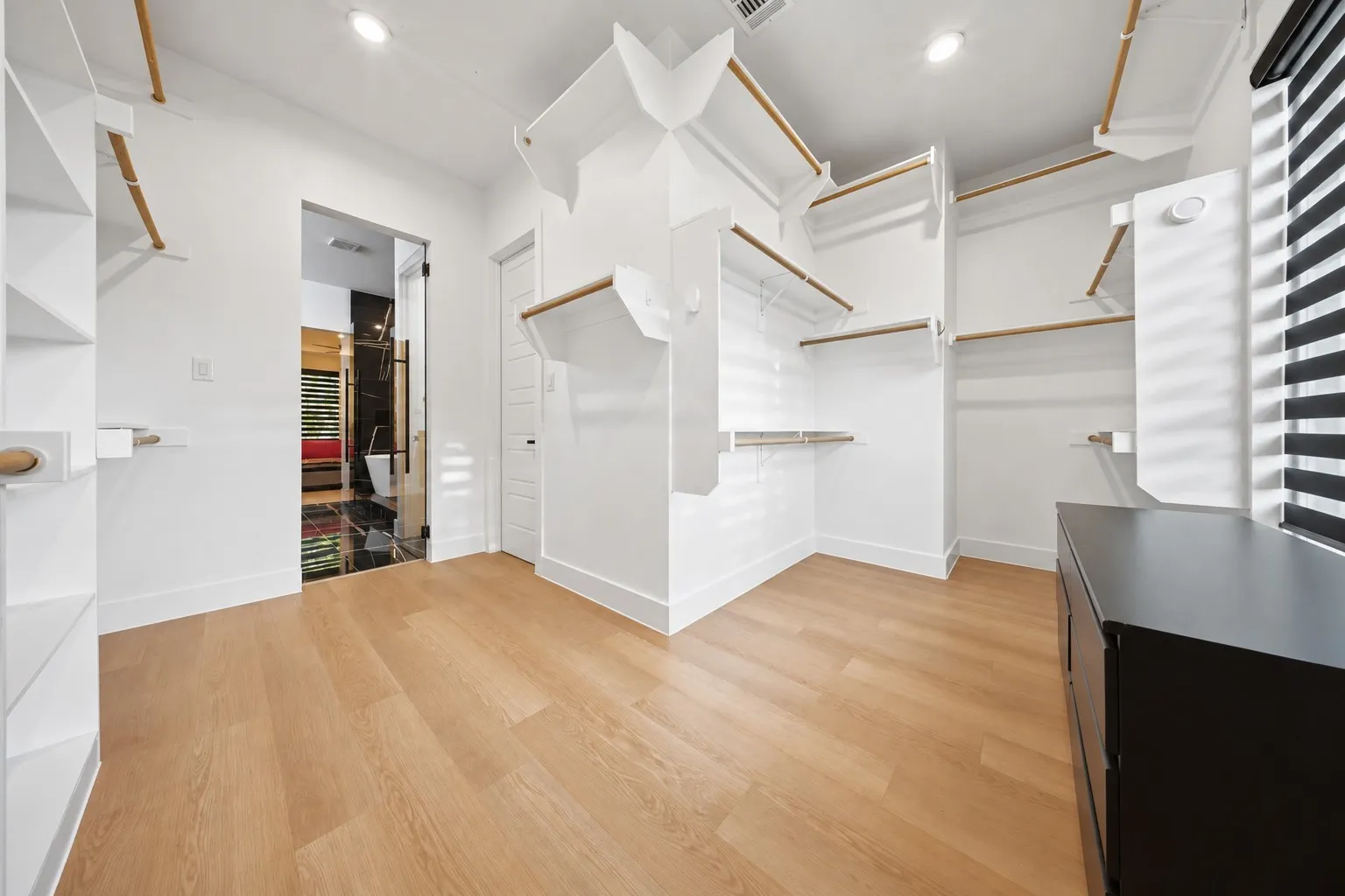 Spacious closet with wood-finish flooring, built-in shelving, integrated hanging rods, recessed lighting, and a dark wood-finish cabinet