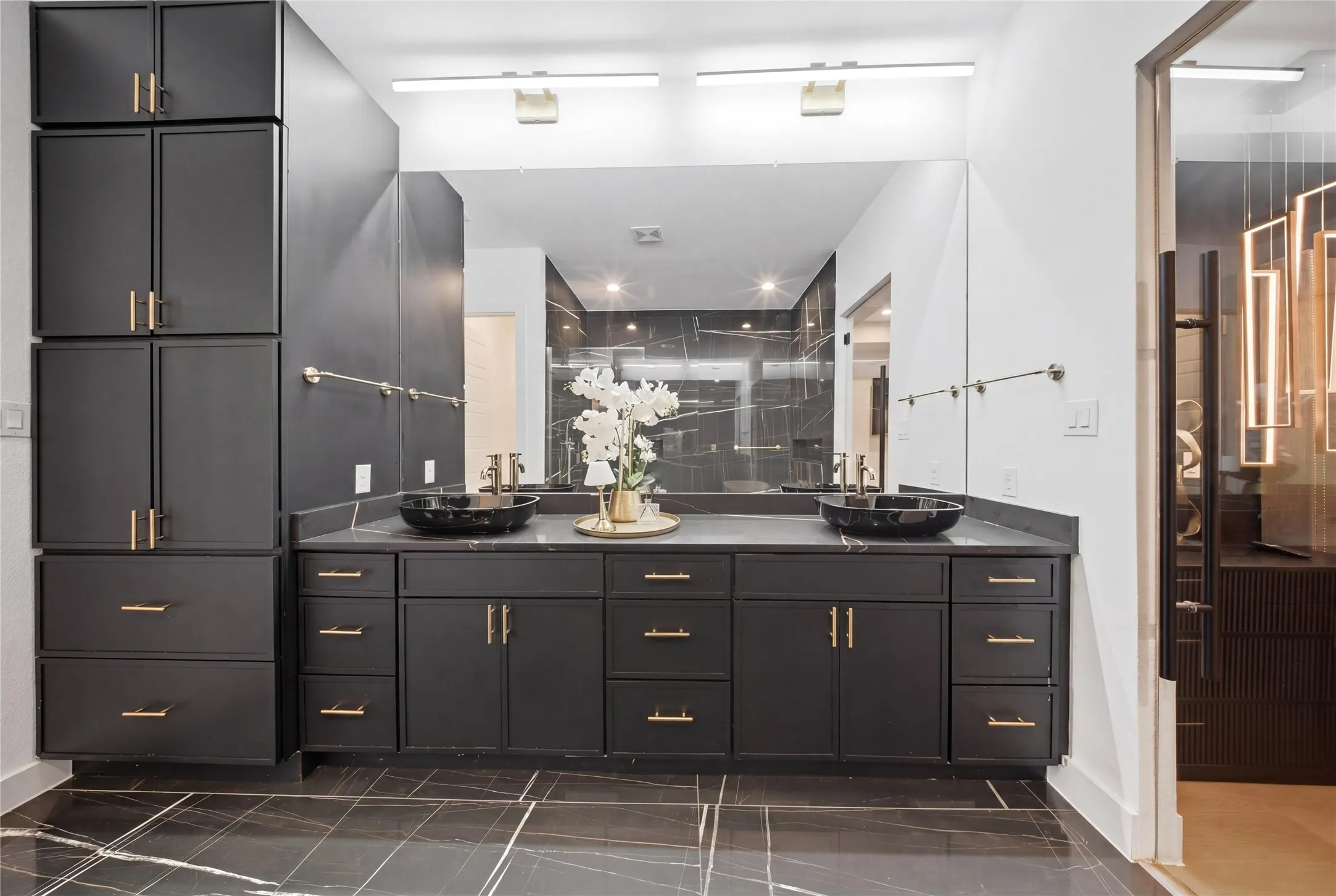 Dual vessel sinks, expansive vanity with extensive cabinetry, full-width mirror, and marble-look floor tiling