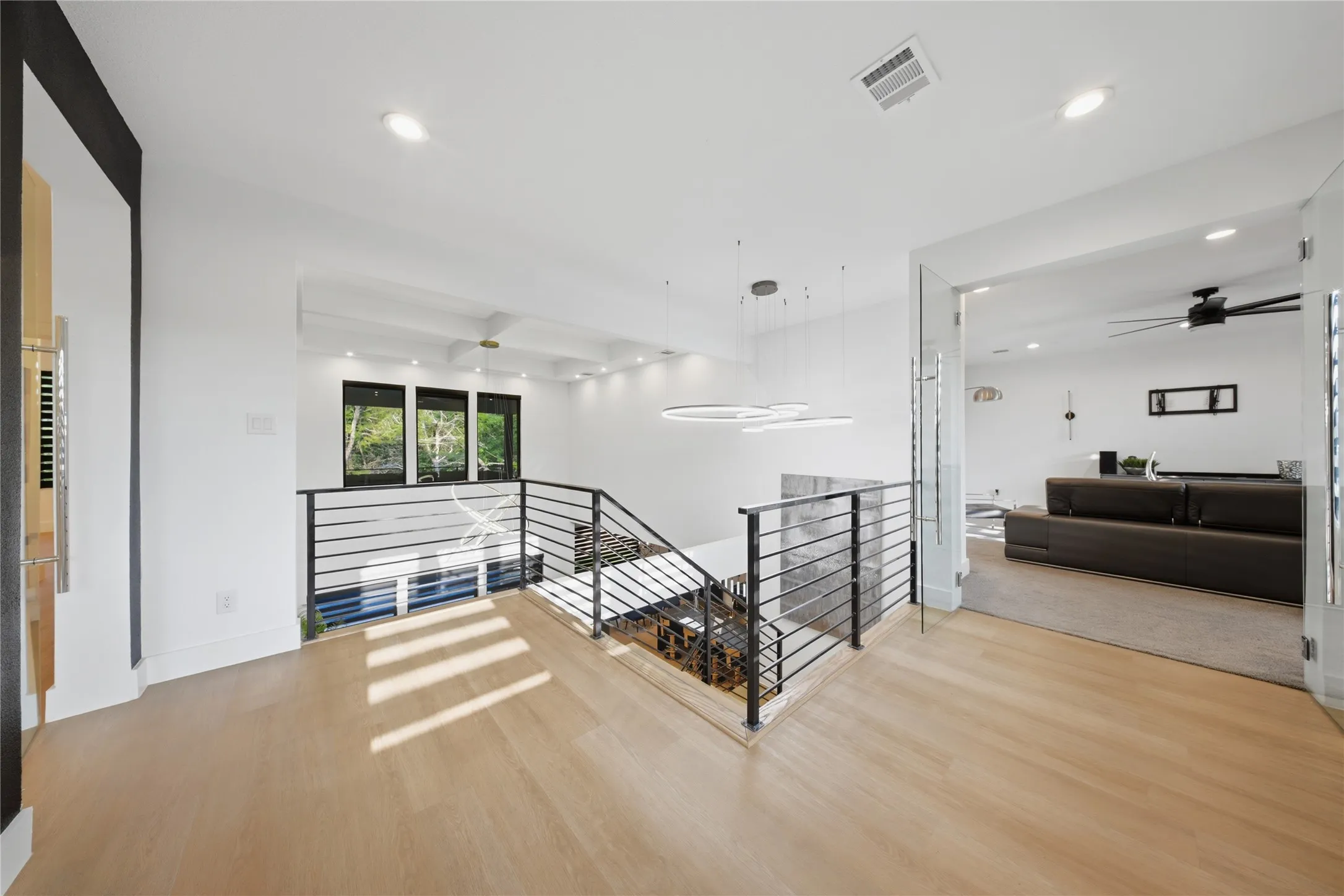 Wood-finish flooring, contemporary staircase with horizontal metal balusters, modern chandelier, recessed lighting, and glass panel entry door
