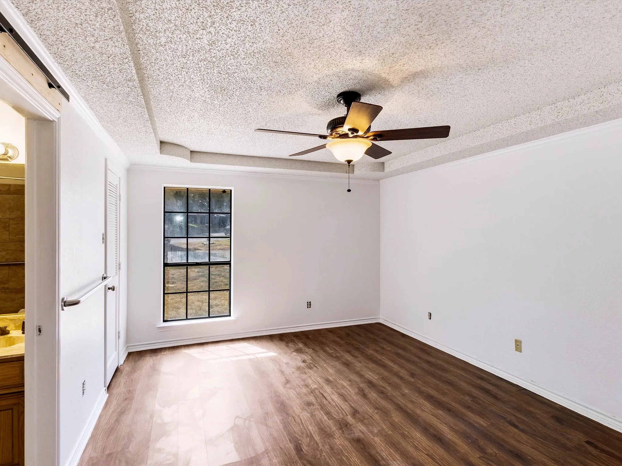 Wood-finish flooring, white walls, tray ceiling, ceiling fan with integrated lighting, and a multi-pane window