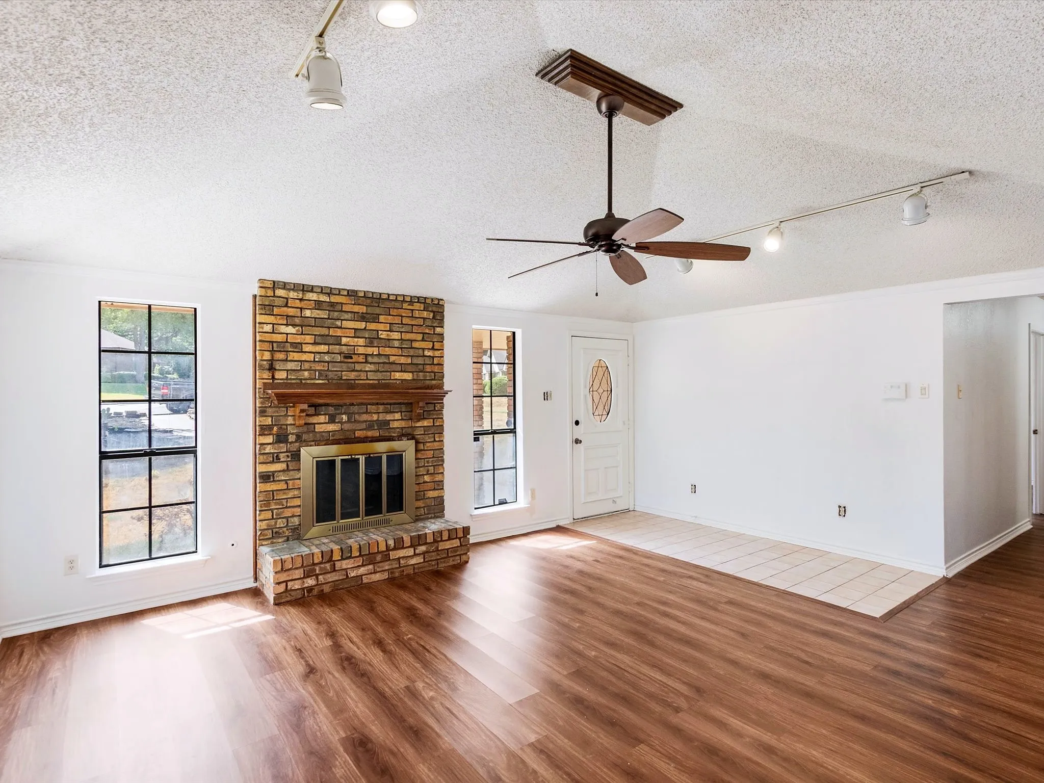 Spacious room featuring wood-finish flooring, a brick fireplace with a wood mantle, and multiple grid-pattern windows