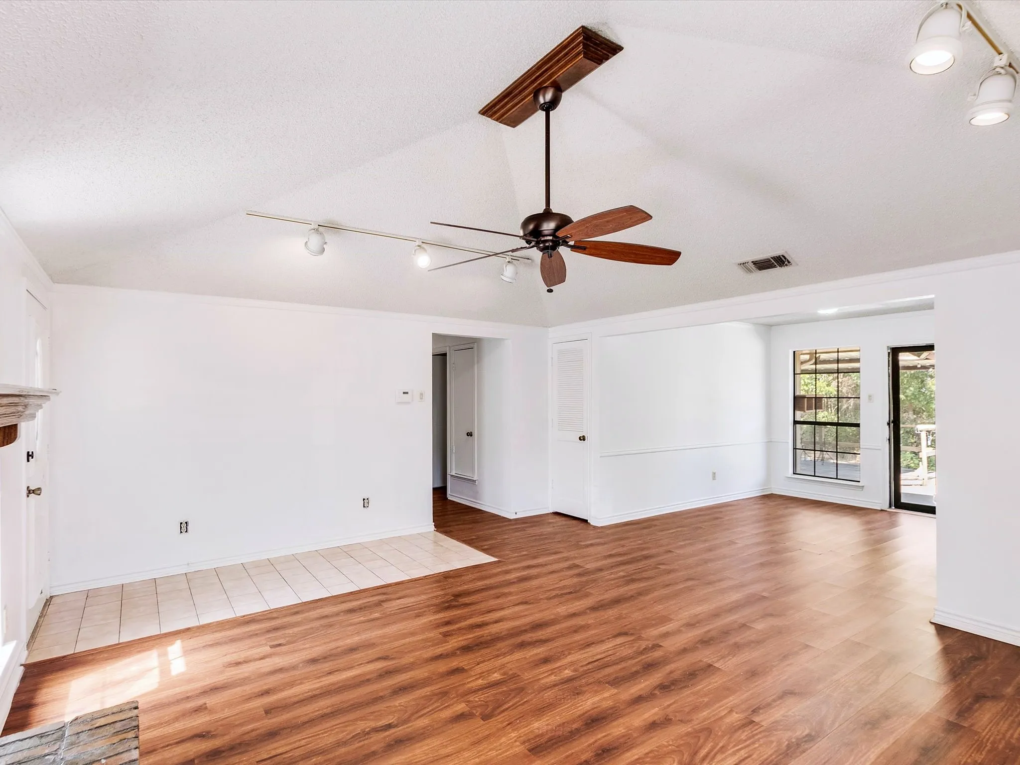 Vaulted ceiling, wood-finish flooring, ceiling fan, track lighting, and a glass-paneled exterior door