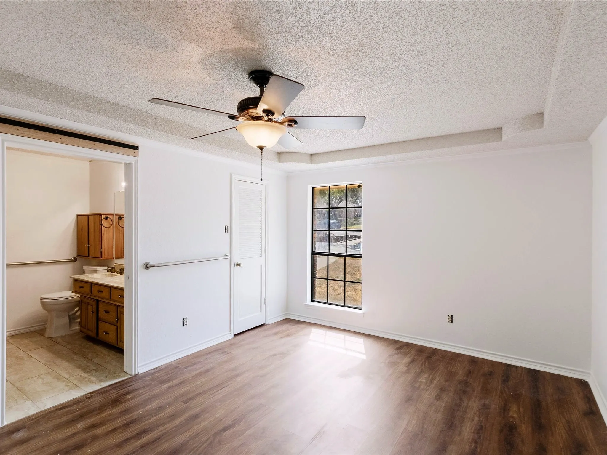 Spacious room featuring wood-finish flooring, a ceiling fan with integrated lighting, and a multi-pane window