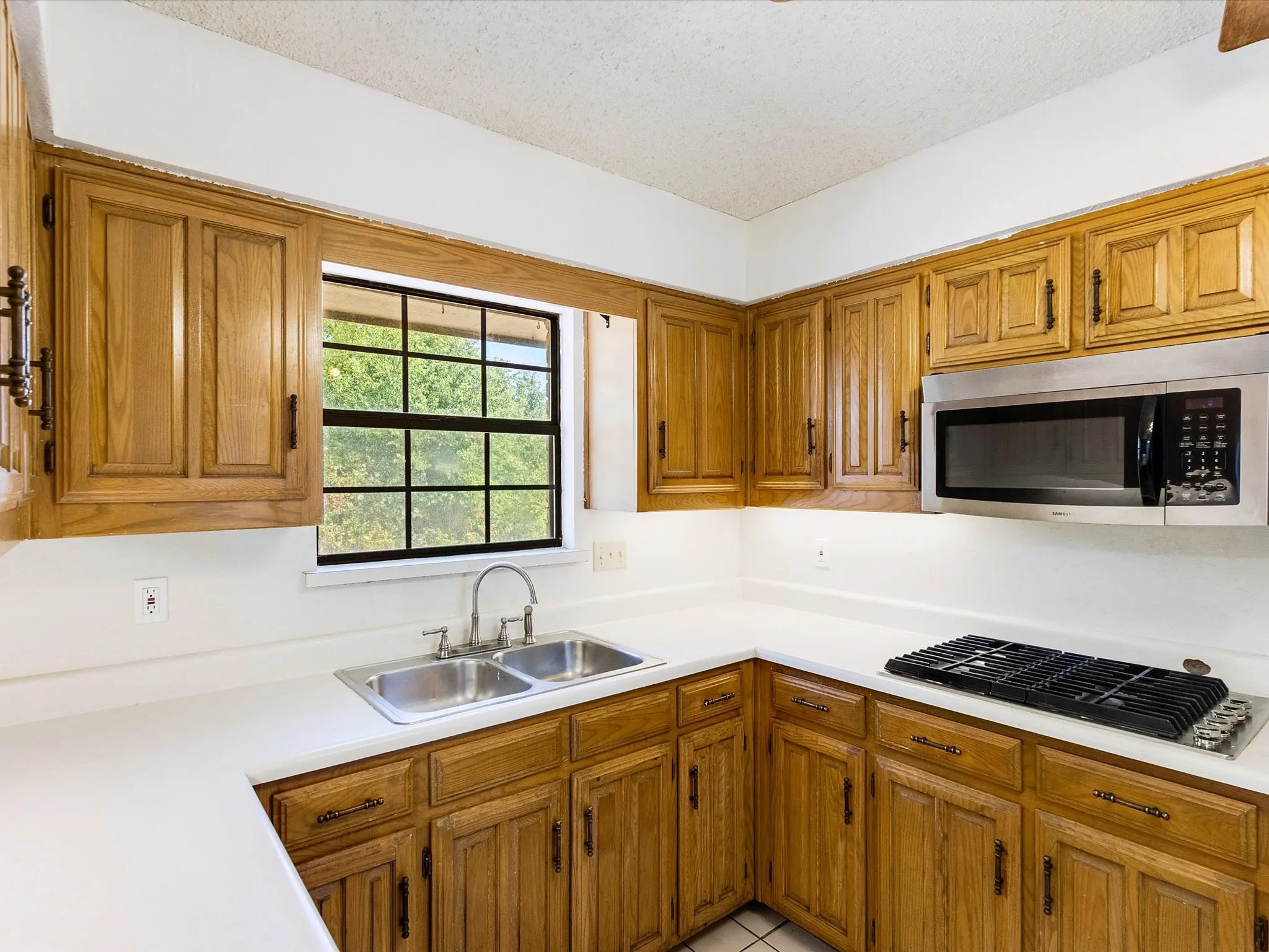 Kitchen with wood cabinetry, white countertops, stainless steel dual basin sink, and an over-range microwave