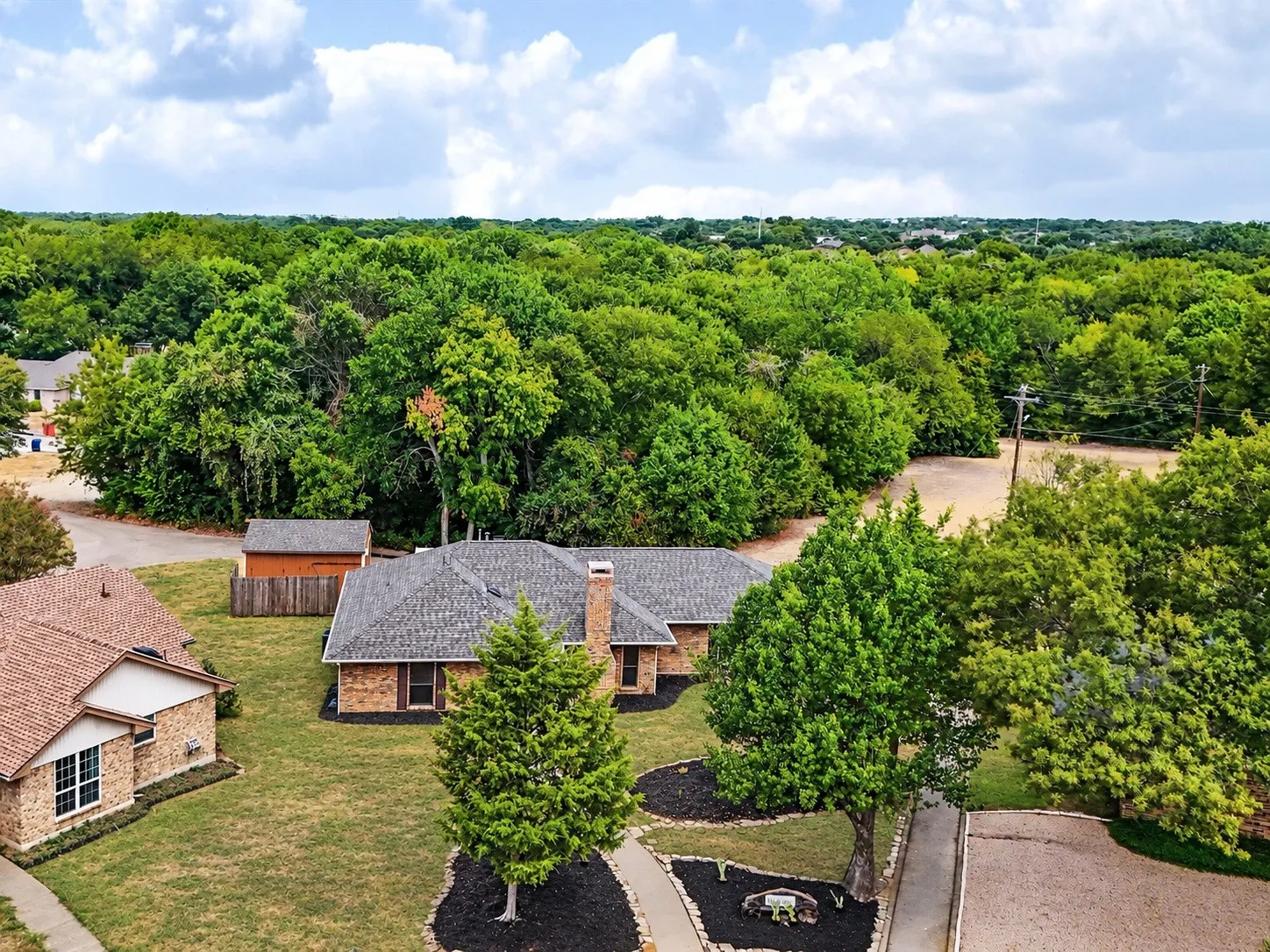 Brick exterior residence with a gray shingled roof, featuring a brick chimney, and a stone-edged walkway