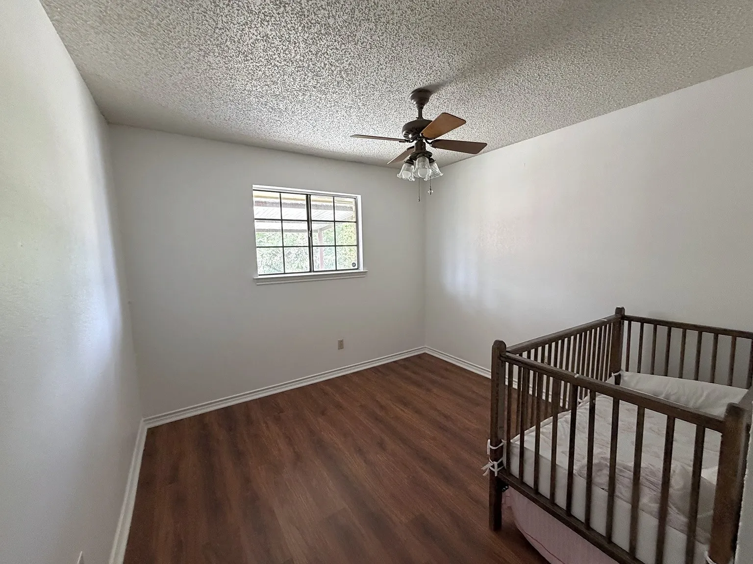 Wood-finish flooring, white painted walls, window with gridded panes, and a ceiling fan with light fixture