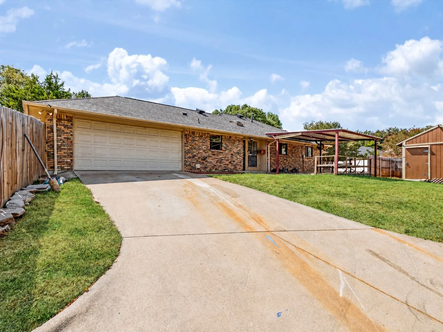 Brick exterior, attached garage, concrete driveway, wood privacy fence, and an outdoor storage shed