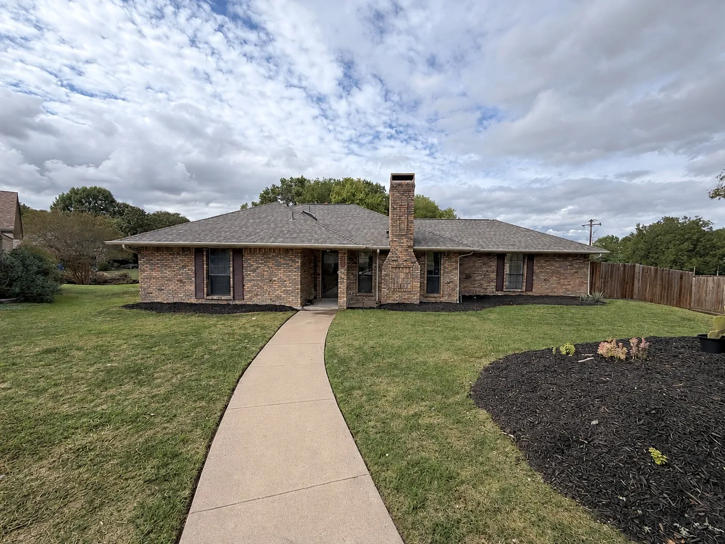 Brick exterior with a prominent brick chimney, gabled roofline, and a concrete walkway