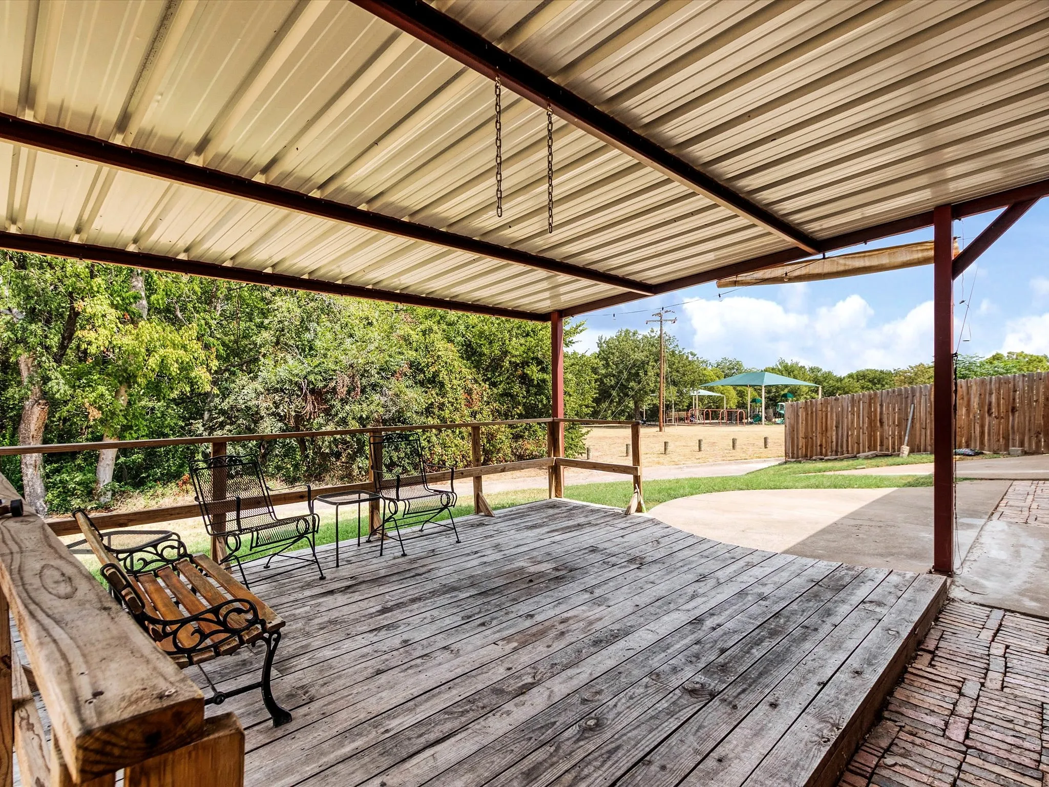 Covered outdoor patio with a corrugated metal roof, wood-plank decking, and a wood railing