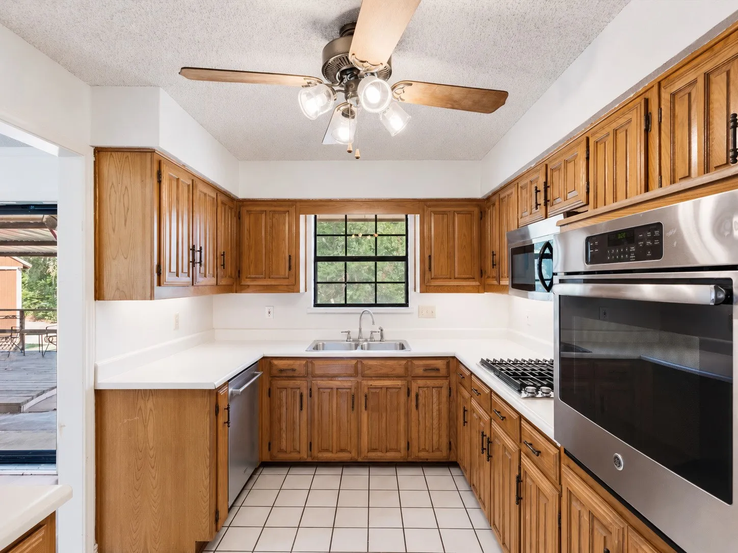 Kitchen featuring wood-finish cabinetry, stainless steel appliances, white countertops, a ceiling fan with integrated lighting, and tile flooring