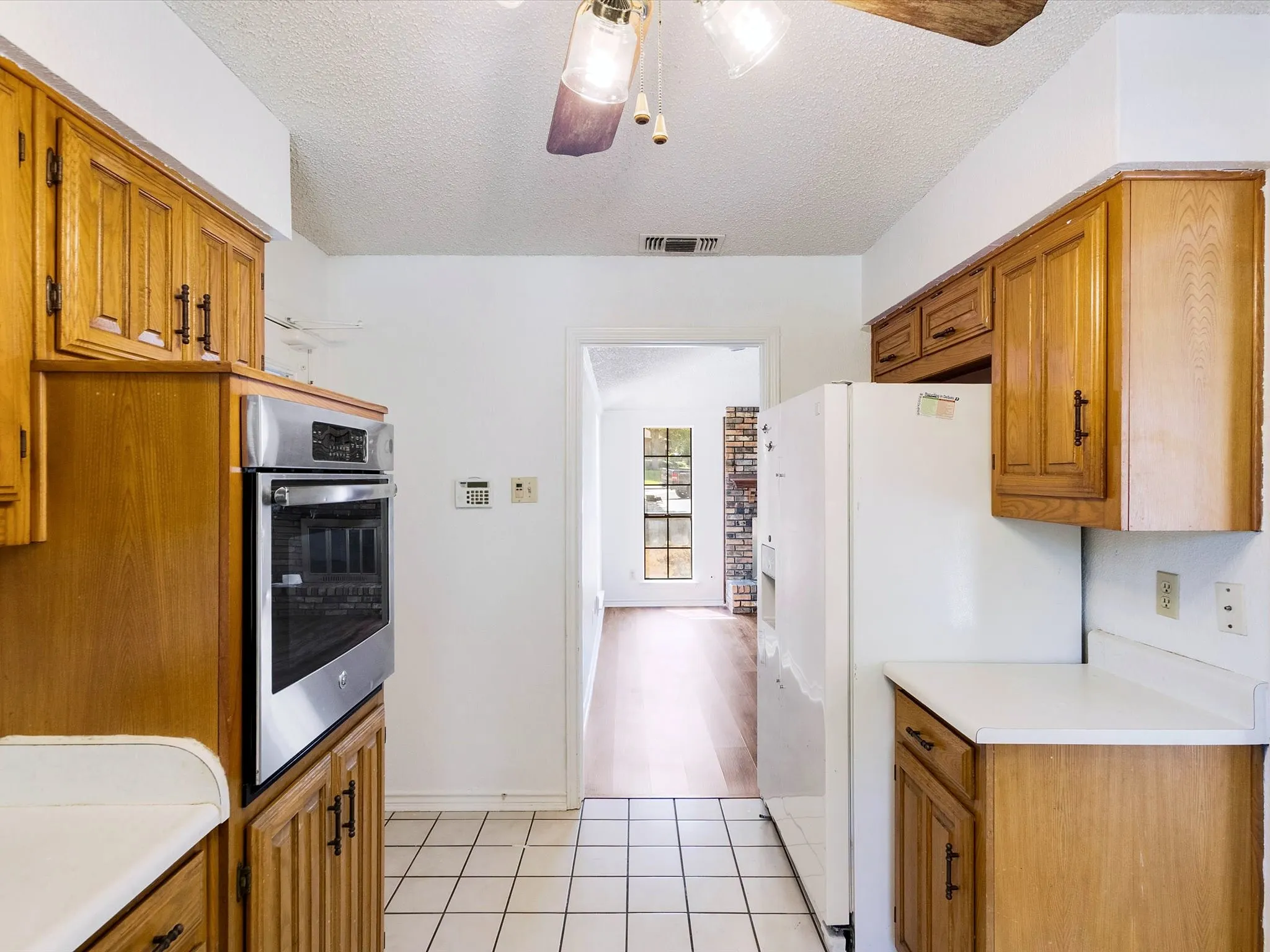 Kitchen featuring a built-in stainless steel oven, wood cabinetry, white countertops, and tiled flooring