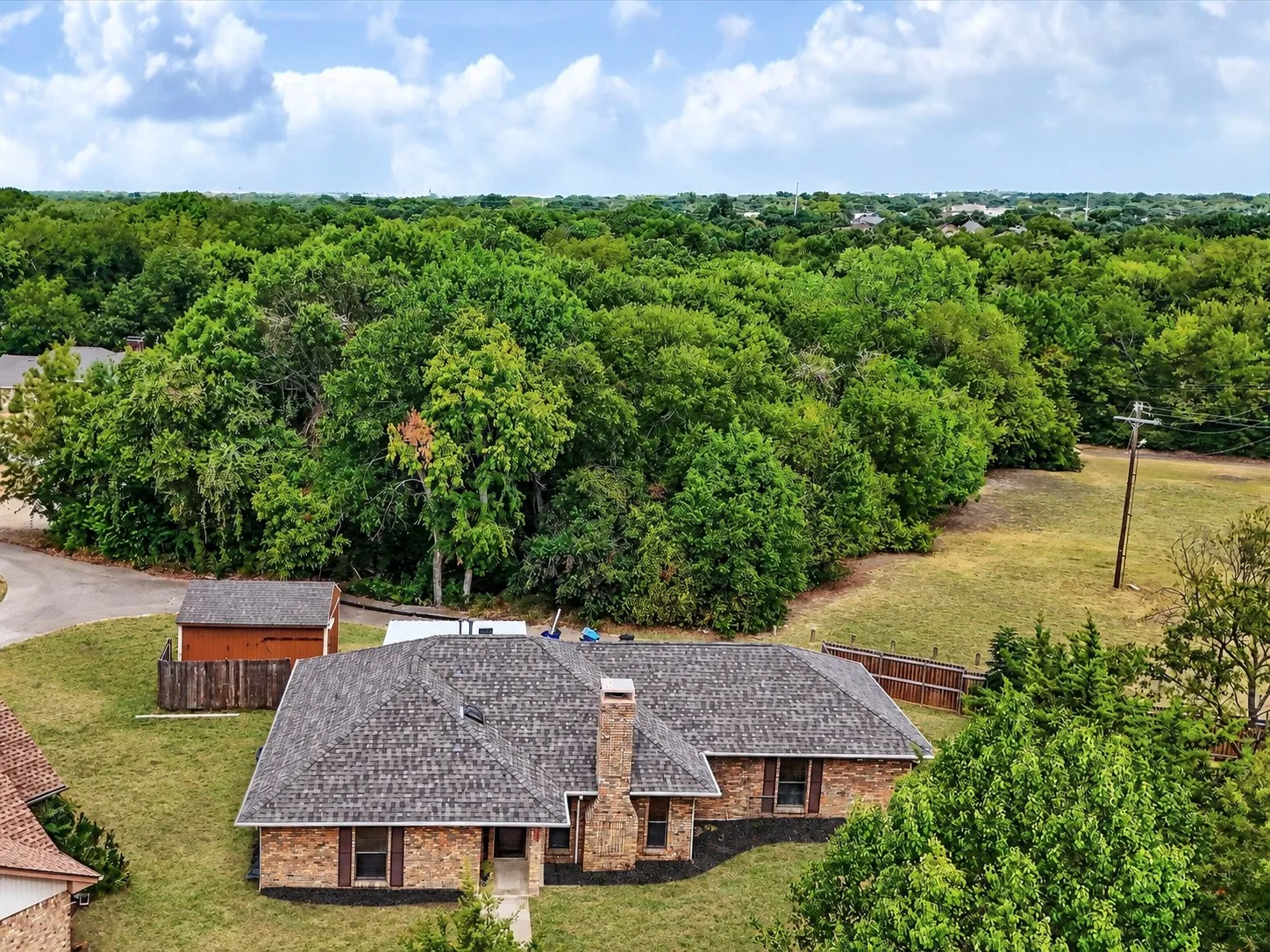Brick exterior with a shingle roof, established landscaping, and a detached shed