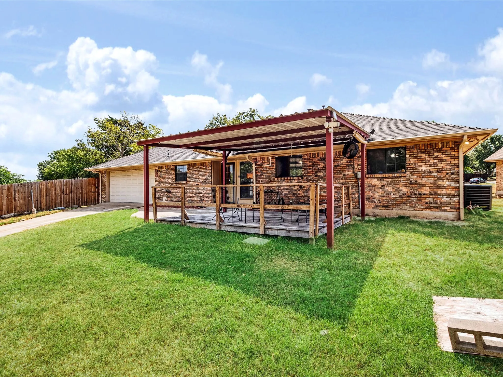 Brick exterior with a covered wooden deck, attached garage, and a fenced yard