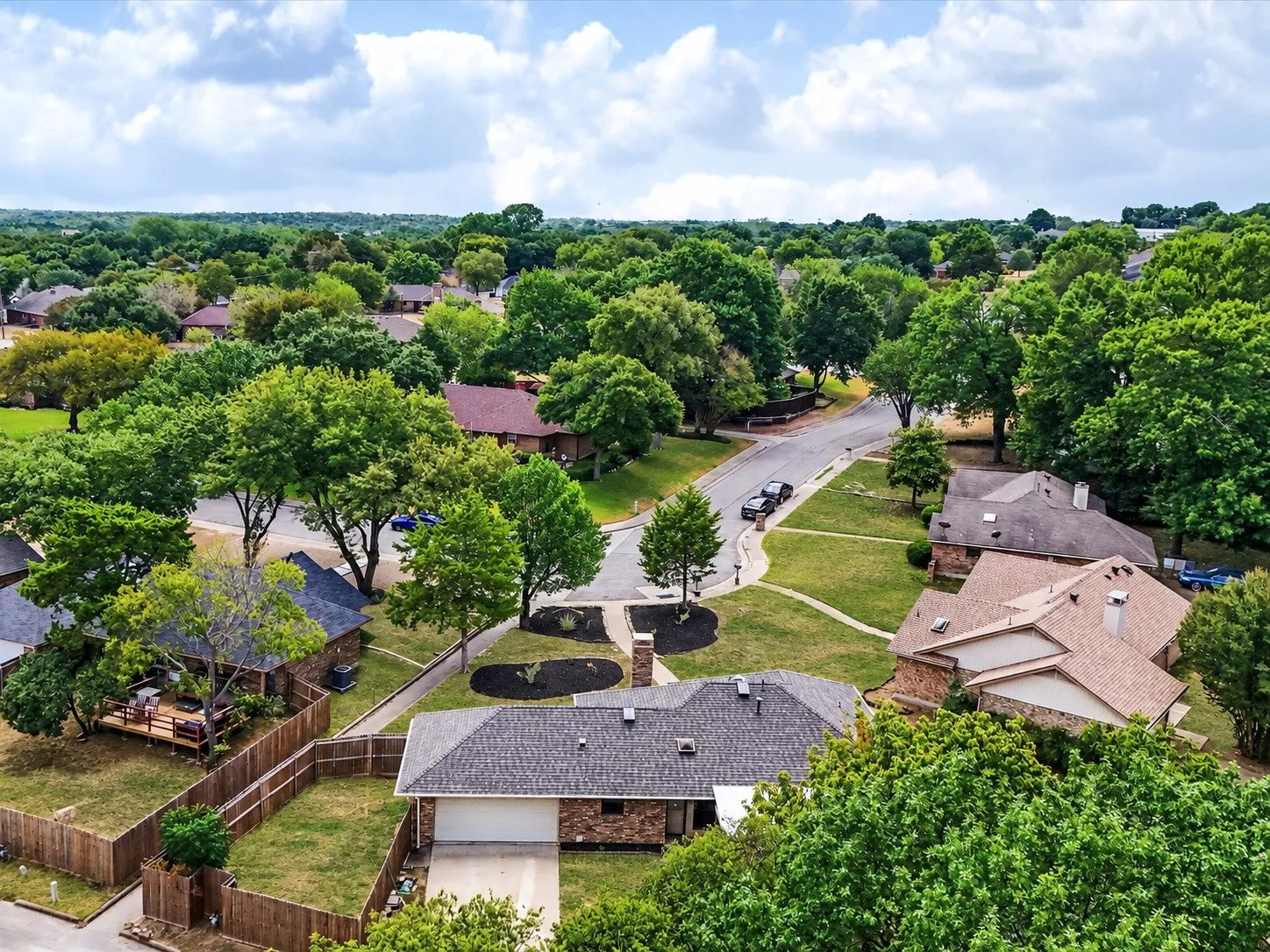 Neighborhood with mature trees, paved streets, and residential properties featuring brick exteriors and shingle roofs