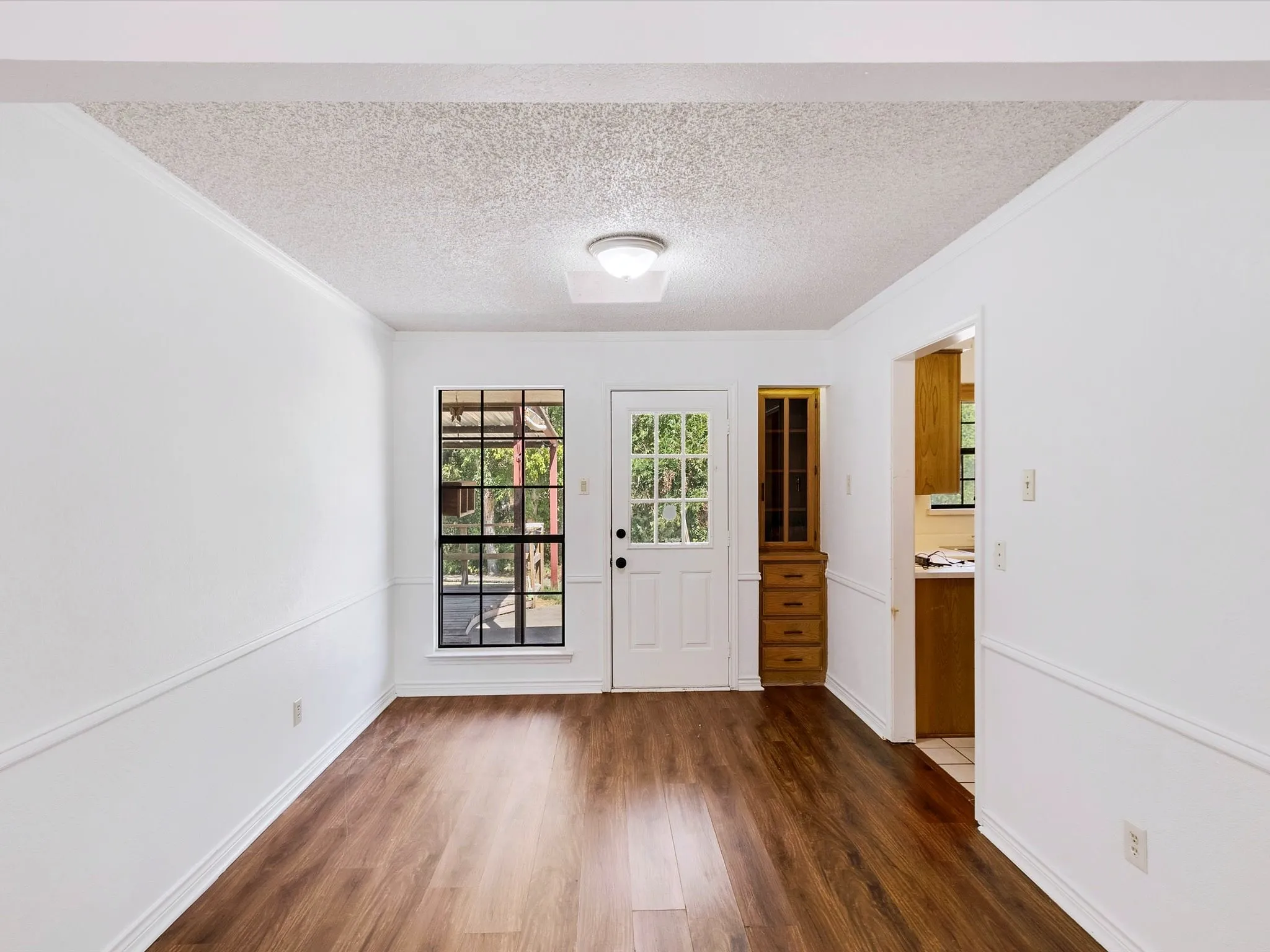 Wood-finish flooring, white walls with chair rail molding, and a built-in wood cabinet